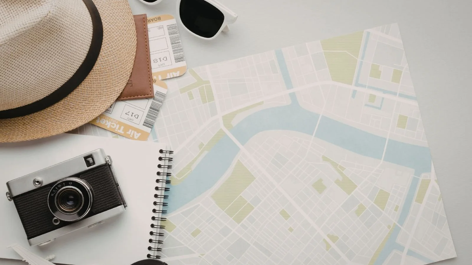 A map, hat, camera, air tickets, and a notebook on a desk used to plan an upcoming vacation.