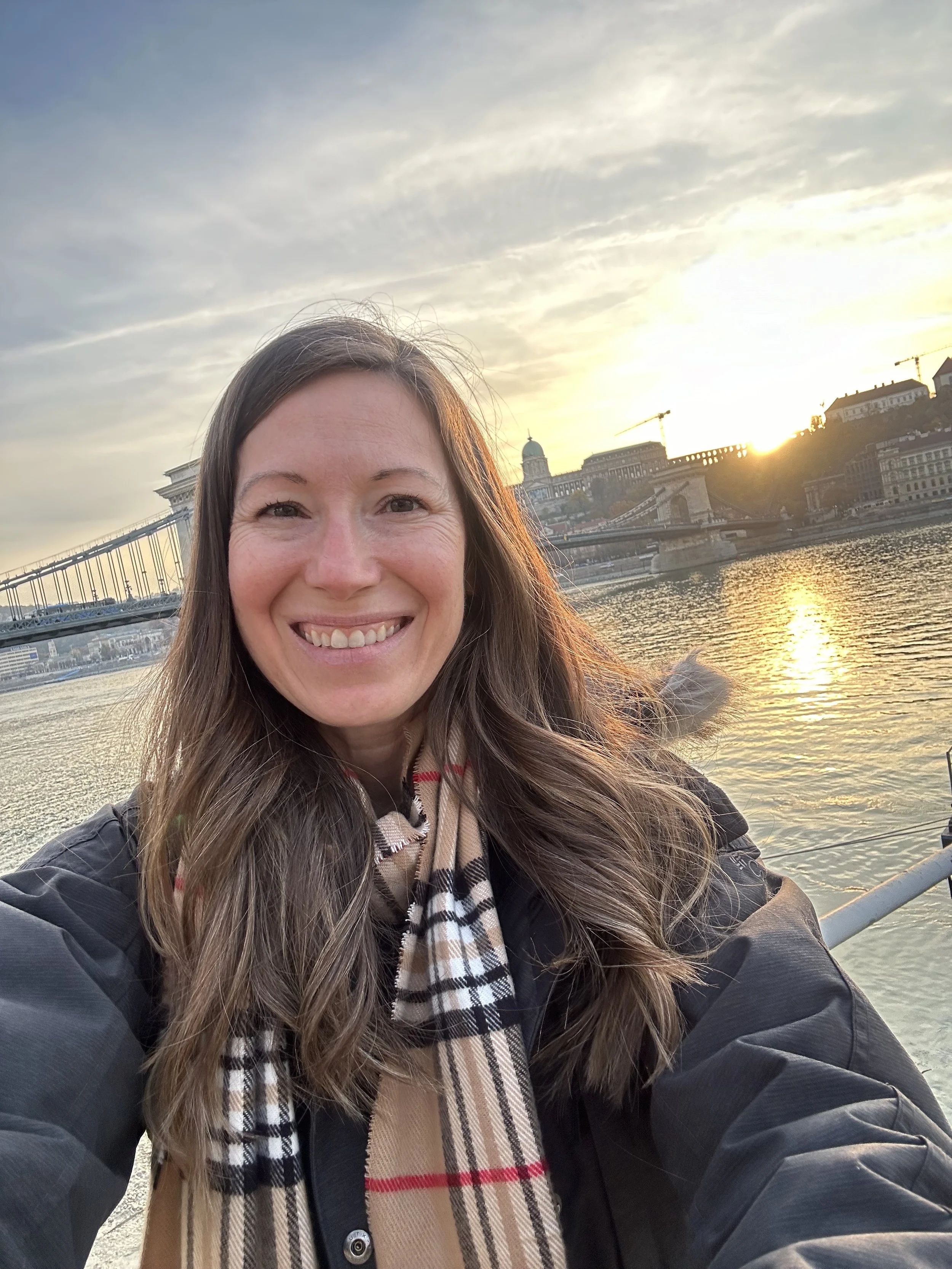 Jaimie Stojanovski from Branch & Bloom Travel LLC in Budapest, Hungary near the river with a bridge and a sunset.