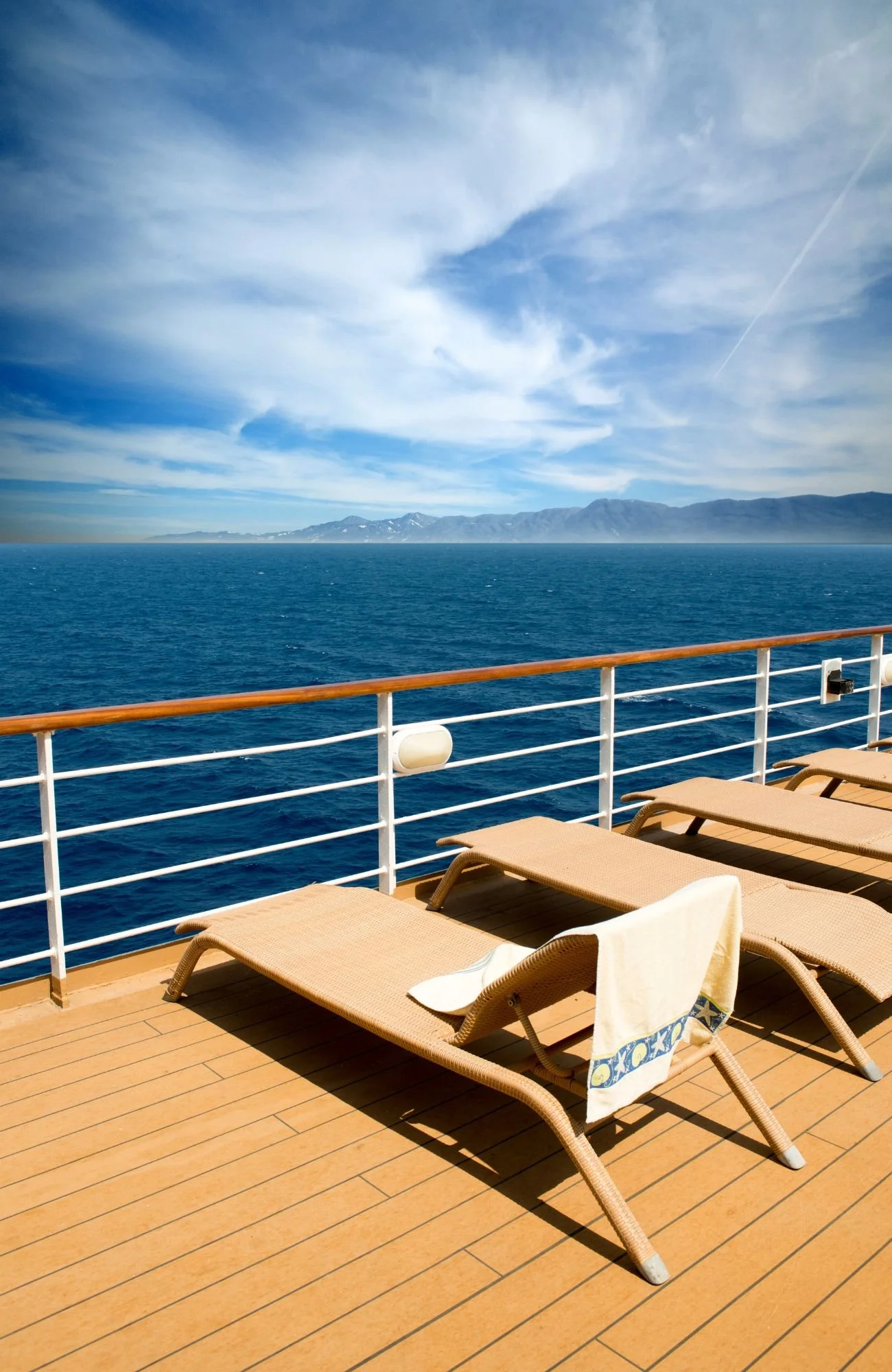 A cruise ship deck with loungers looking out over the blue water with land in the background
