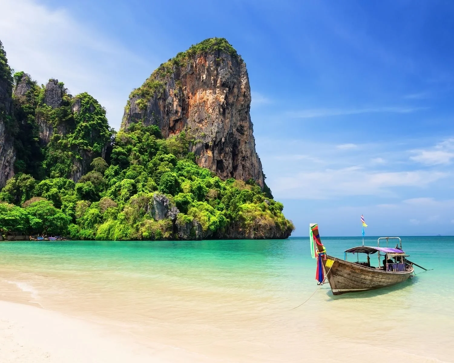 Railey Beach in Thailand that shows the bright blue waters and a longtail boat.