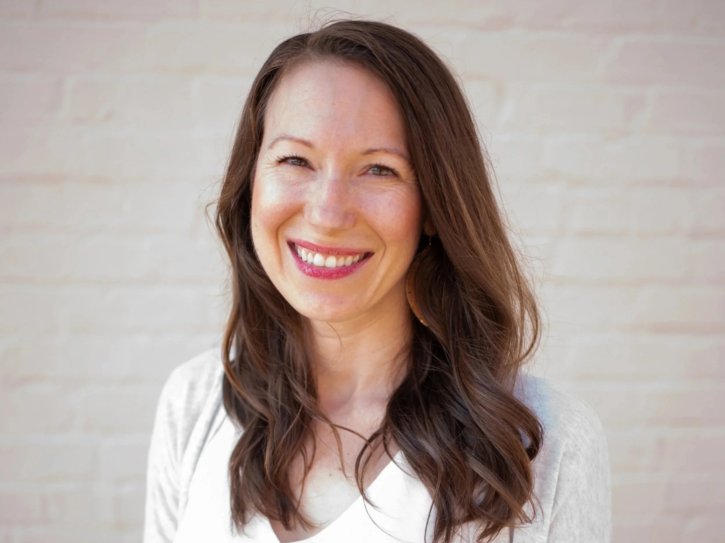 The Branch and Bloom Travel LLC owner, Jaimie Stojanovski's headshot in front of a white brick background.