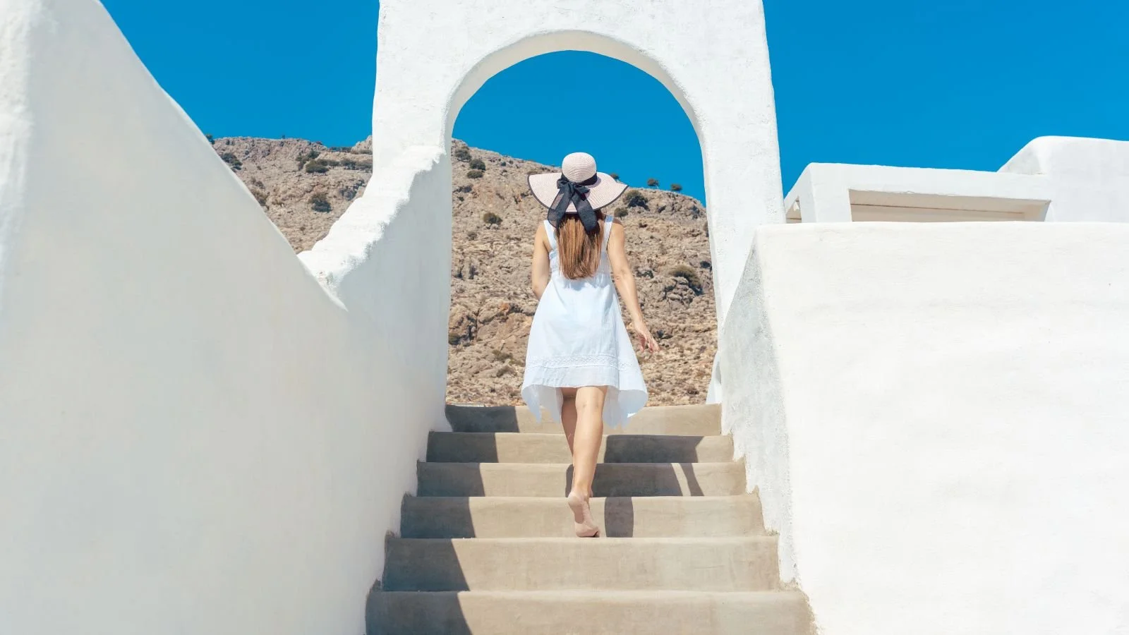 A woman walking up the stairs in Greece imagining how to choose a vacation destination.