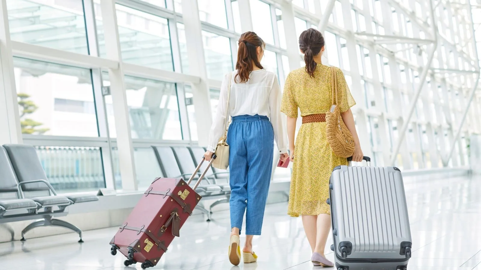 Two travelers walking through an airport with passports and rolling luggage.