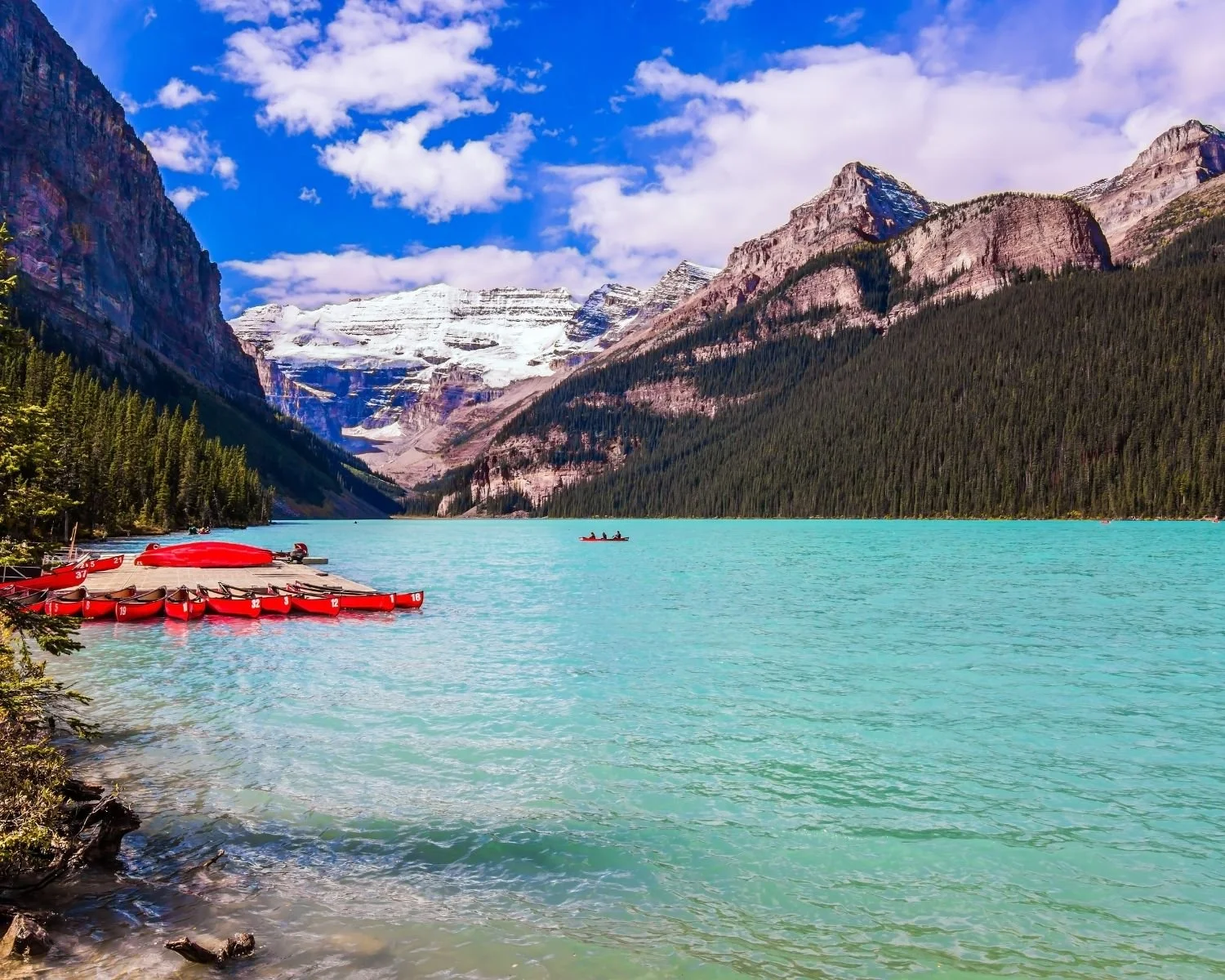 Red canoes on Lake Louise surrounded by mountains in Canada