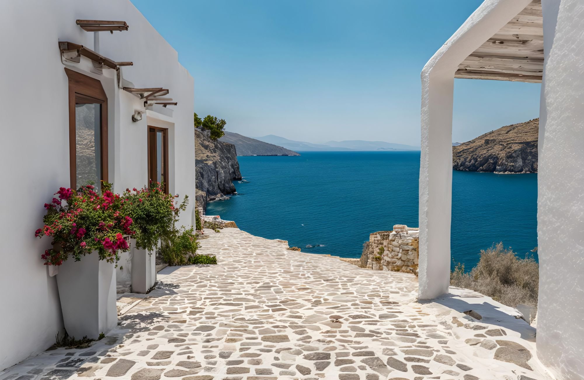A white Grecian village with white buildings, white cobblestone, and flowers, overlooking the water.