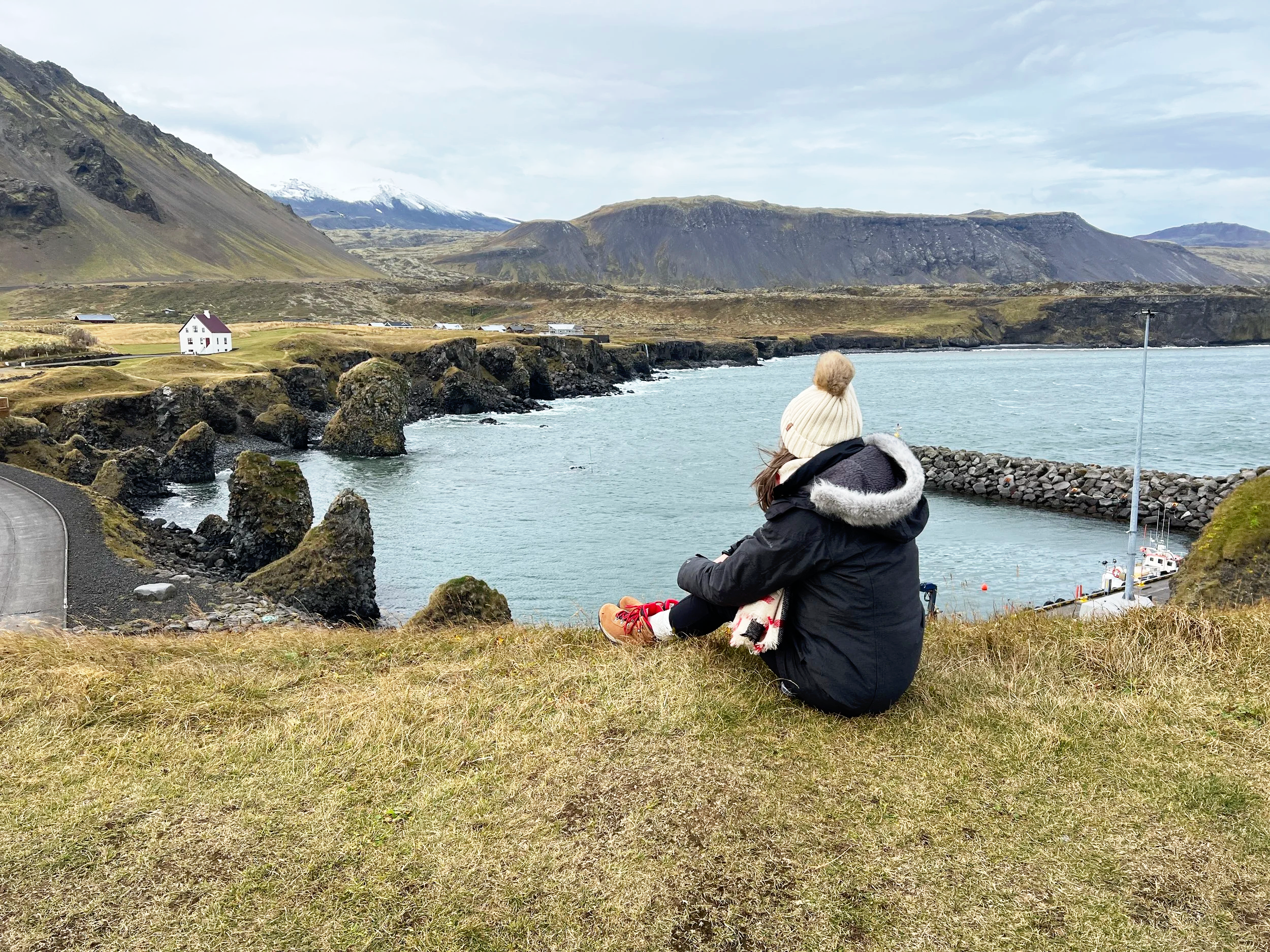 Jaimie owner of branch and bloom travel sitting on the grass in Iceland overlooking water and mountains.
