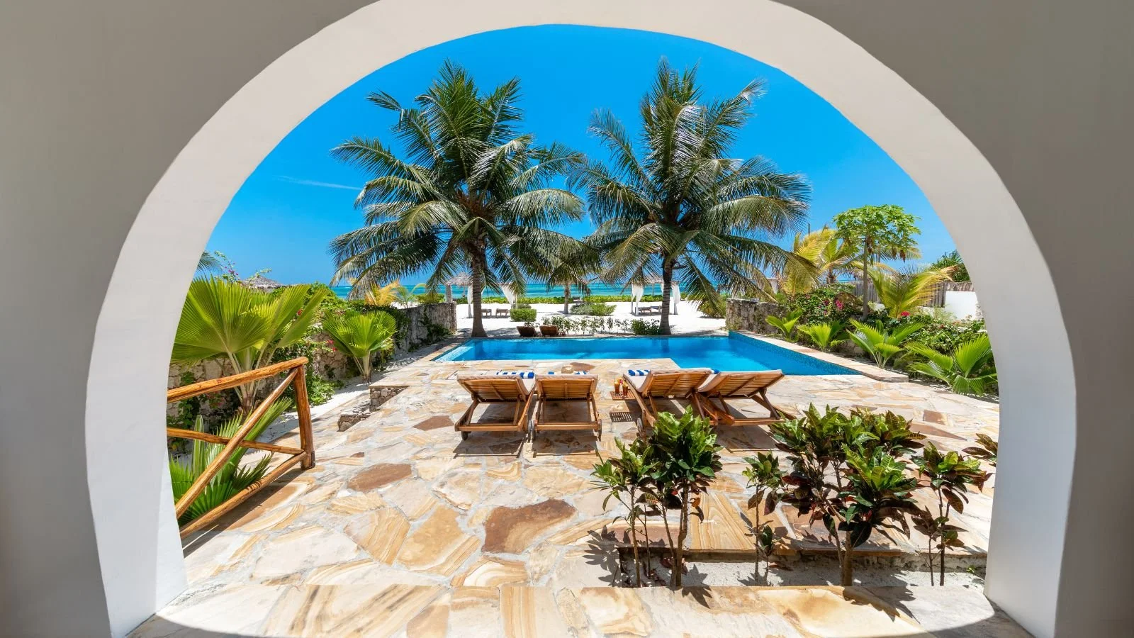 Private pool overlooking a tropical beach, palm trees, and the ocean at a luxury resort.