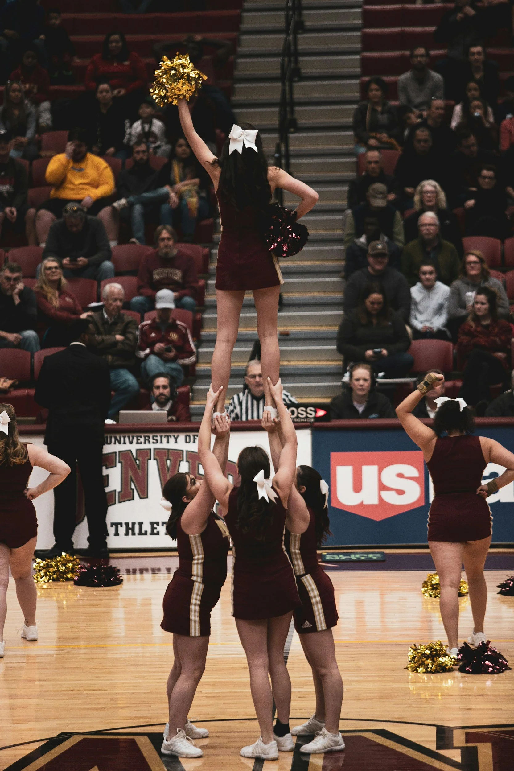 Cheerleader stunt team performing a routine on a basketball court with fans watching from the bleachers.