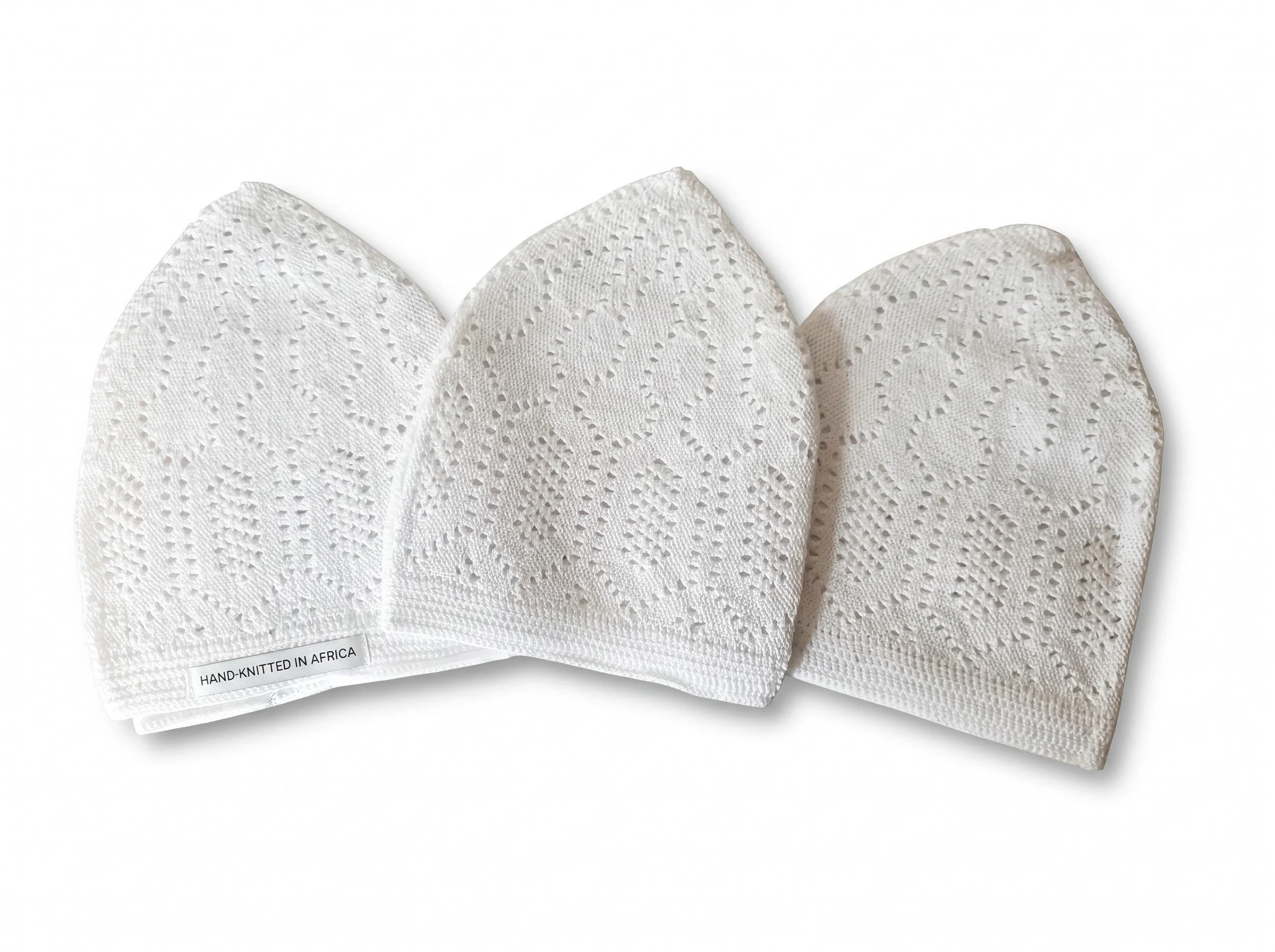 Three white paper napkins with a textured, eyelet design. The napkin on the left has a small label that reads "HAND-KNITTED IN AFRICA."