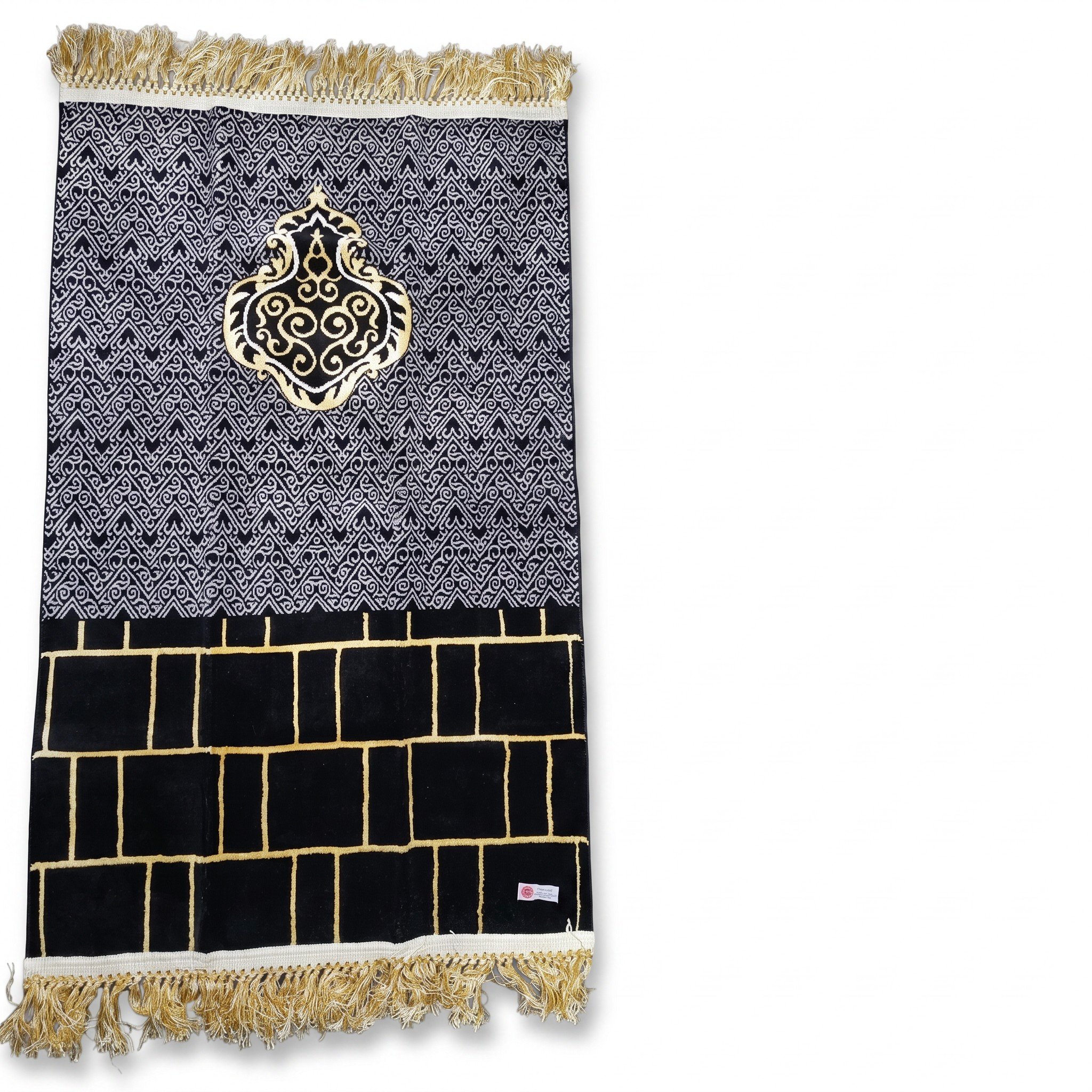 A textile piece with intricate black and gold geometric patterns, fringed edges, and a label at the bottom right corner.