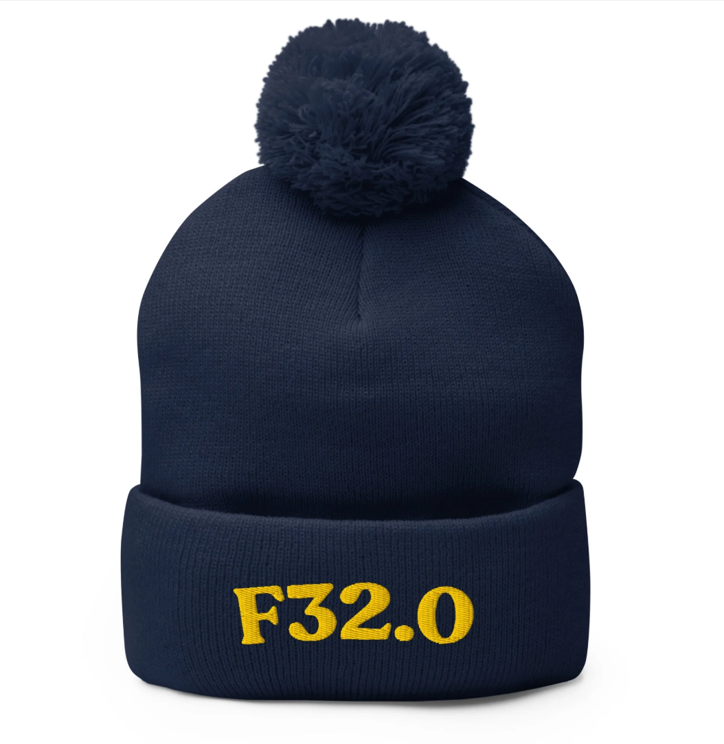 Navy blue knit beanie with a pom-pom on top and yellow embroidered text 'F32.0' on the front