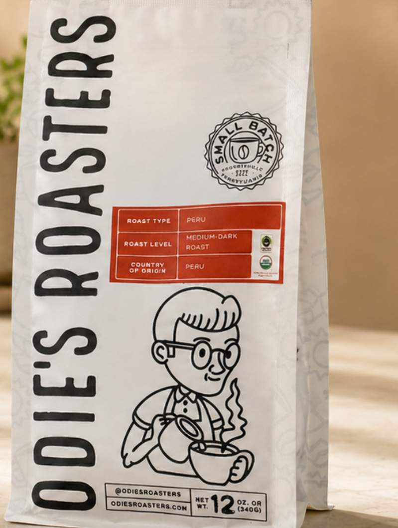 Coffee bag labeled "Odie's Roasters" featuring a cartoon character holding a steaming cup of coffee, with a red label indicating Peru medium-dark roast, 12 oz weight.