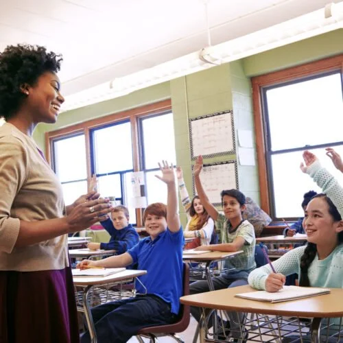 Teacher leading a classroom with students raising hands during a lesson.