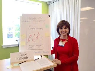 Woman in red blazer standing next to a presentation board in a classroom or conference room
