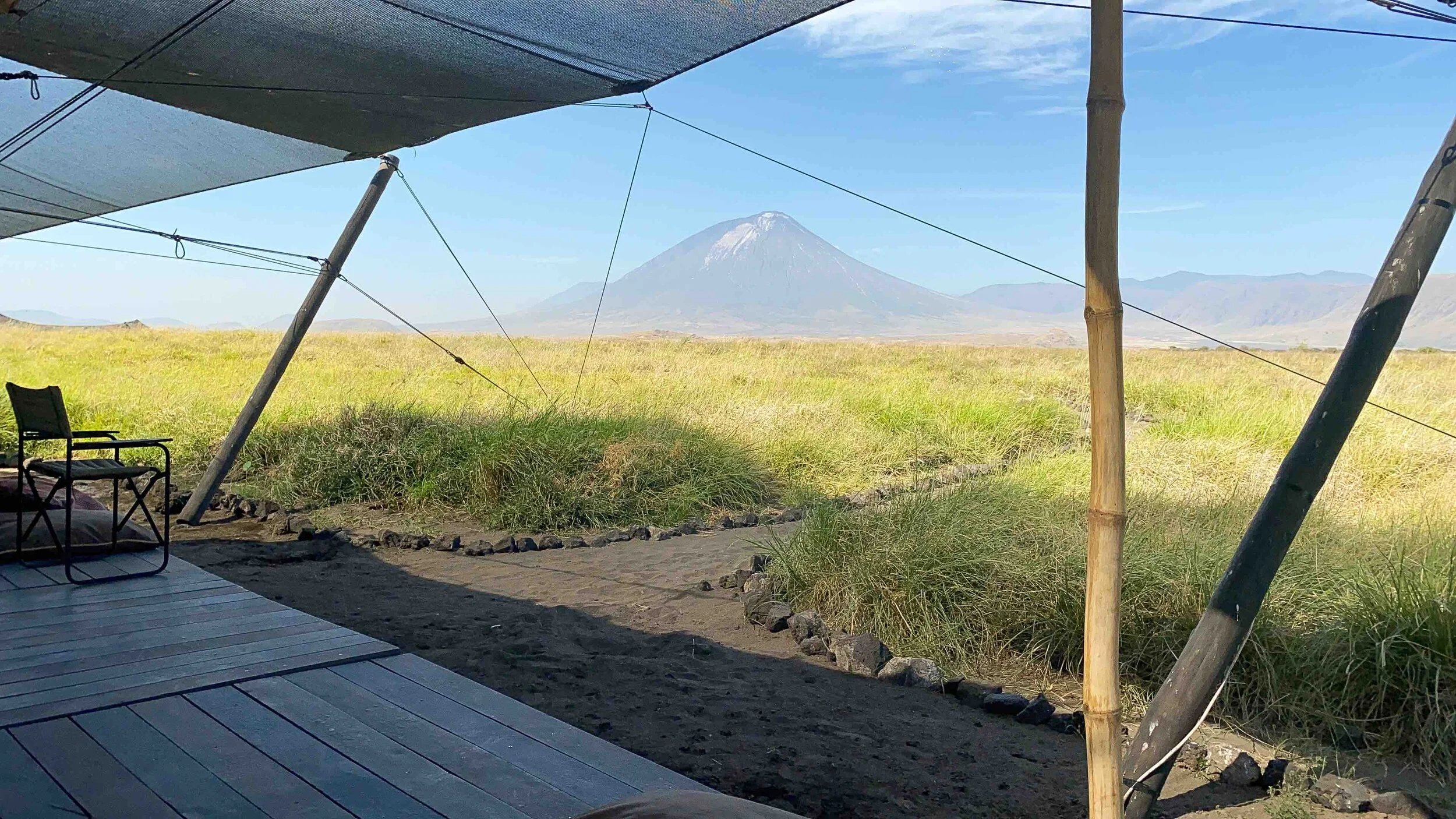 Tent set up on a grassy plain with a view of a mountain in the background and a chair on a wooden deck in the foreground.