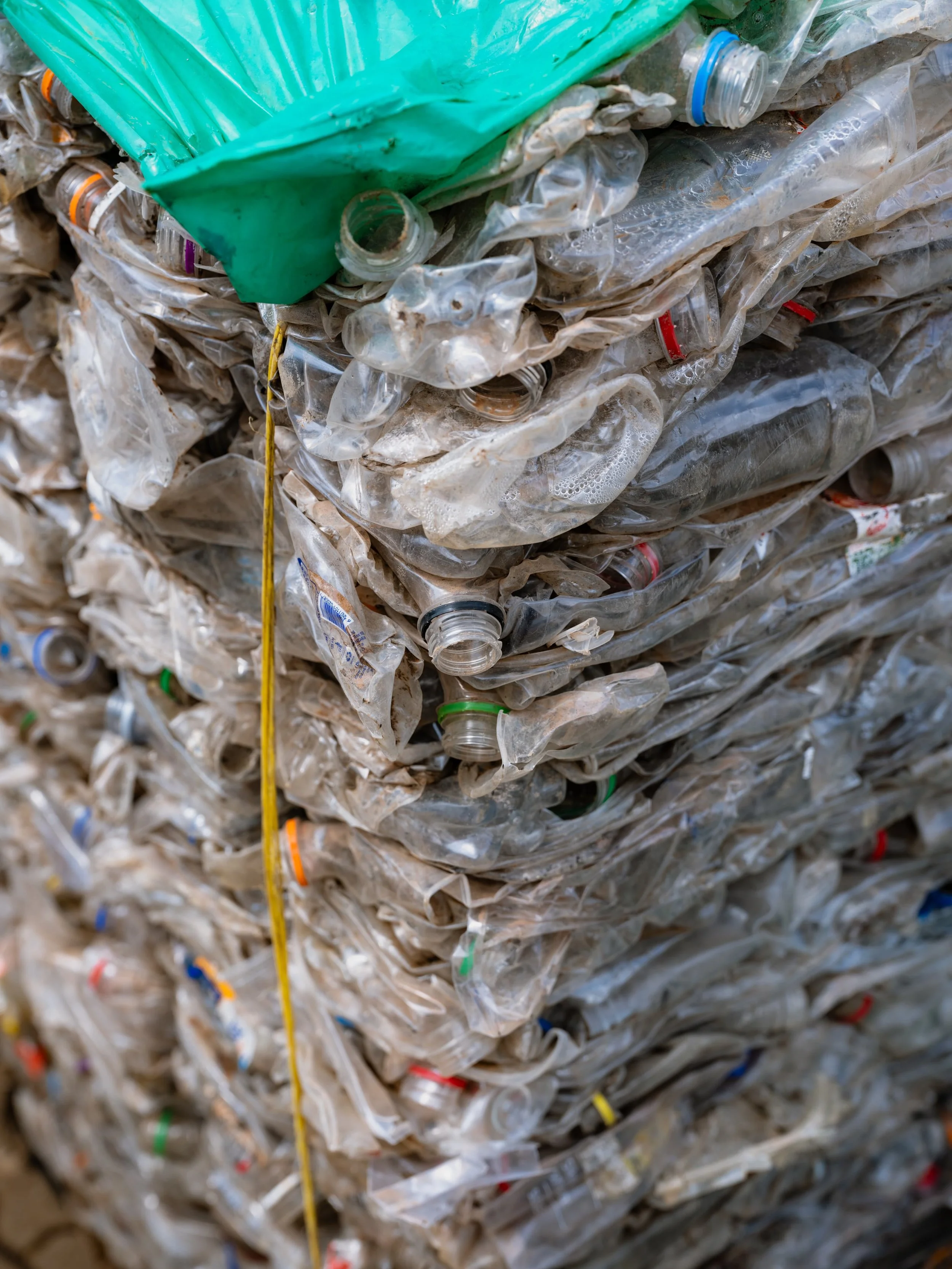 Stacks of crushed and flattened plastic bottles, some with caps attached, piled together with a yellow string running through part of the pile.