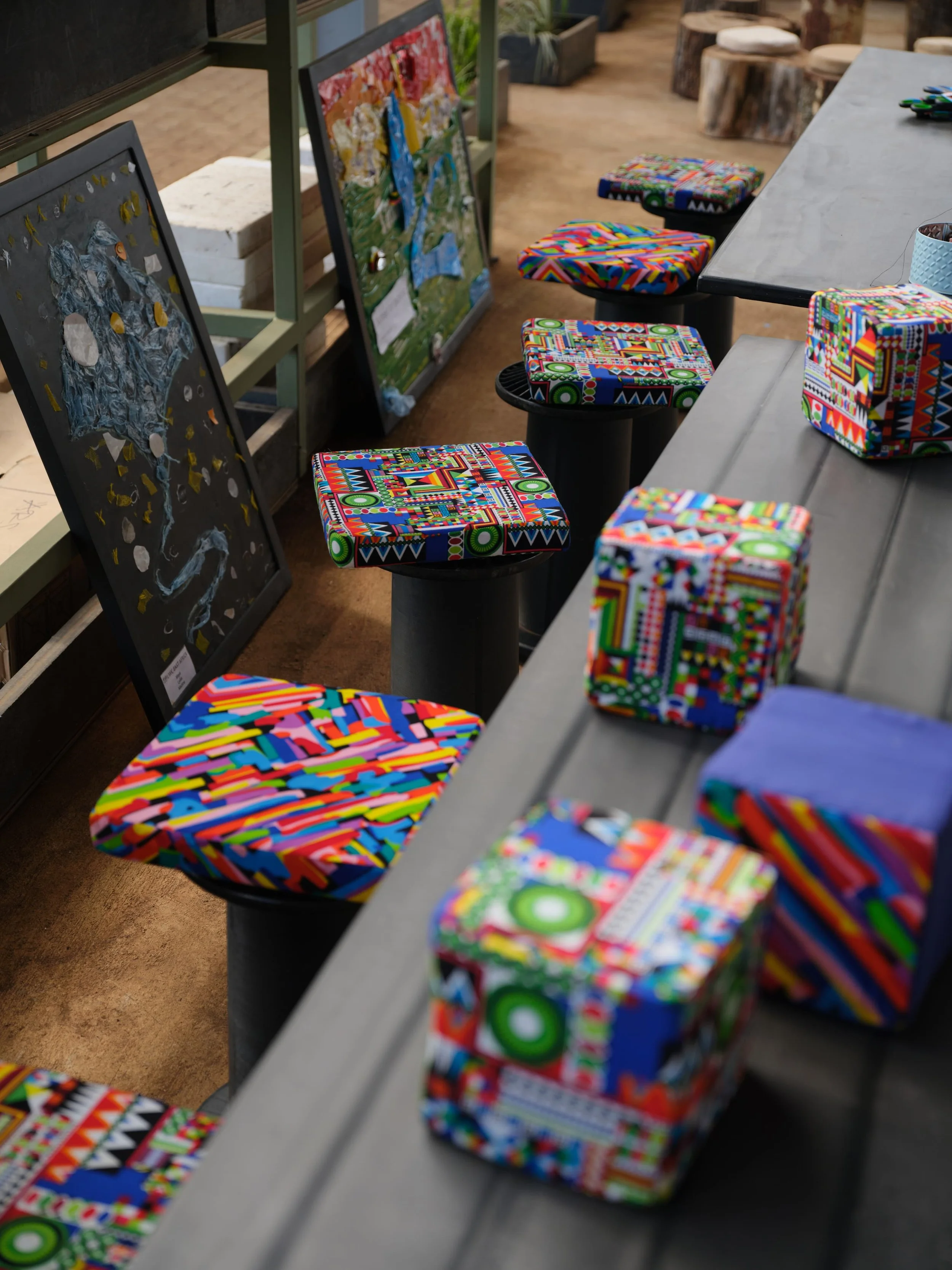 Colorful fabric-covered chairs and small wrapped boxes on a gray table at an art or craft display.
