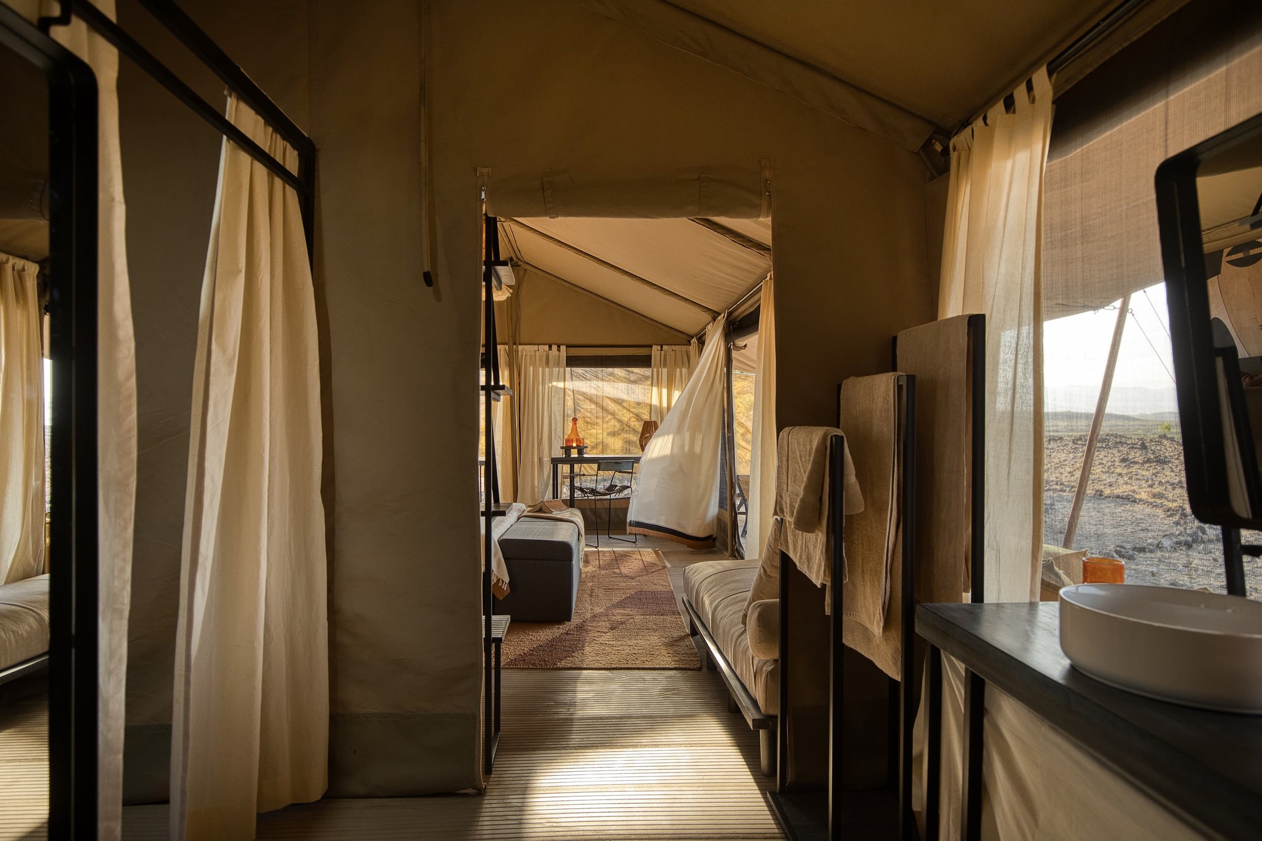 Interior view of a glamping tent with curtains, a seating area, and a view of an outdoor landscape.