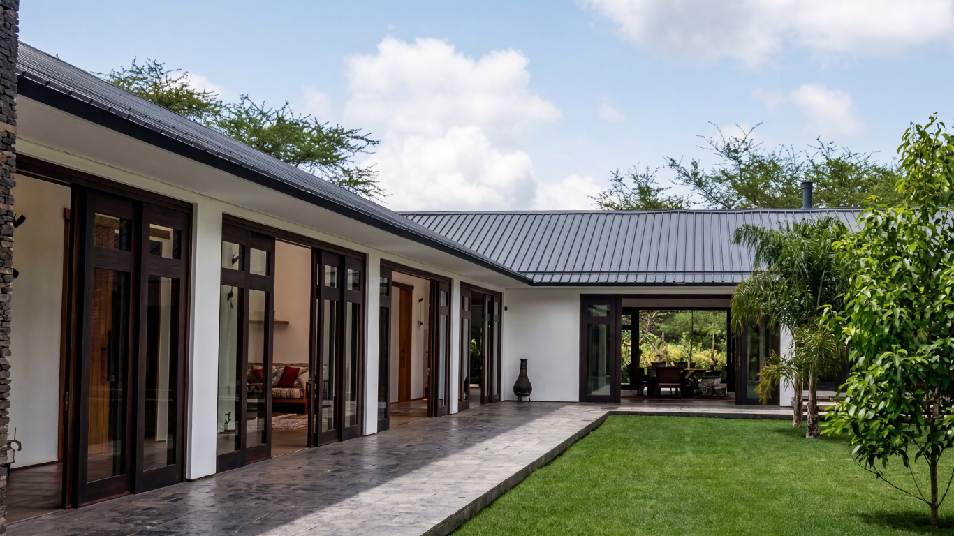 Modern house with sliding glass doors, a sitting area, and a backyard with green grass and trees under a partly cloudy sky.