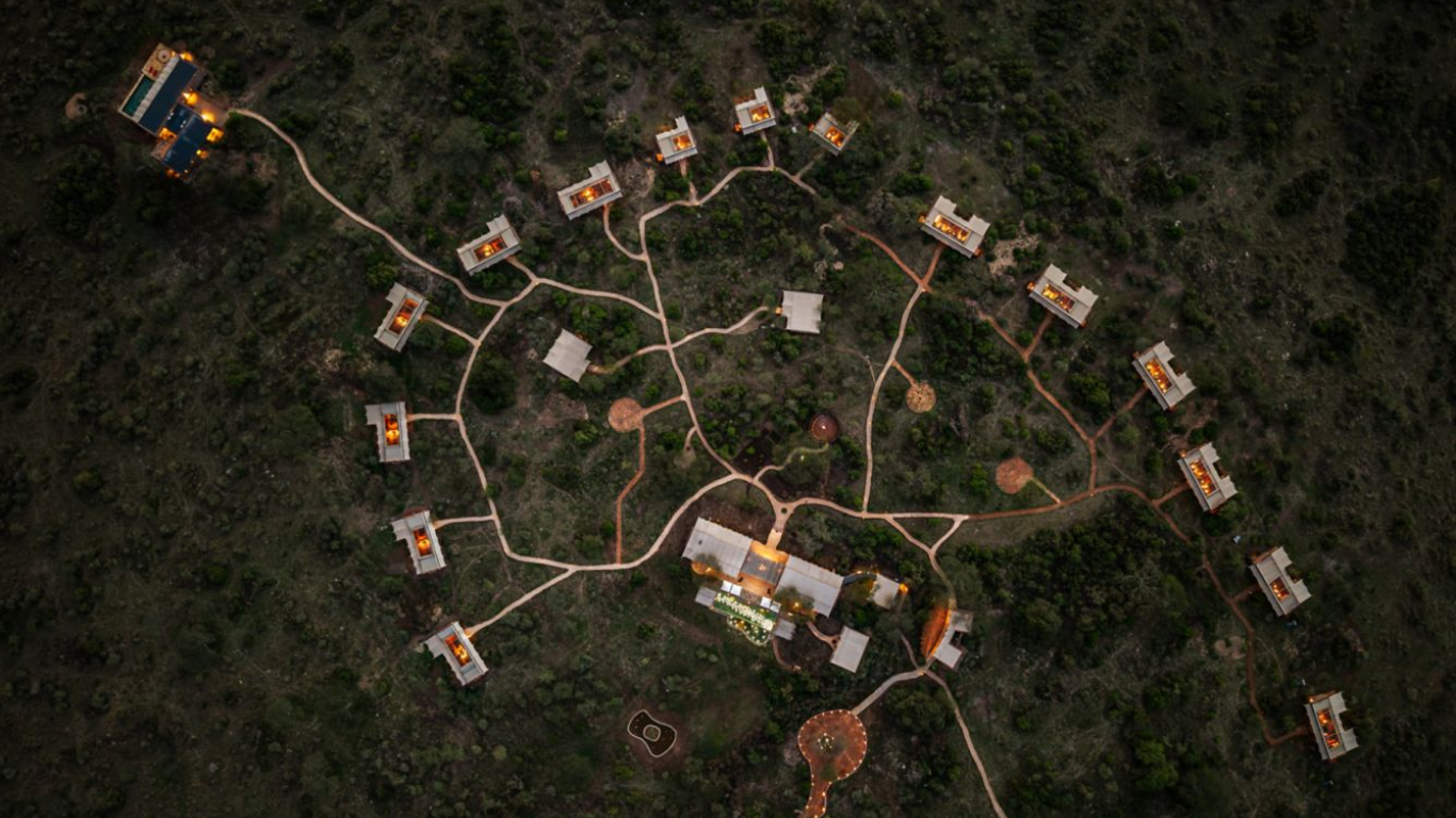 An aerial view of a hillside resort with multiple buildings connected by winding pathways, illuminated at night surrounded by greenery.