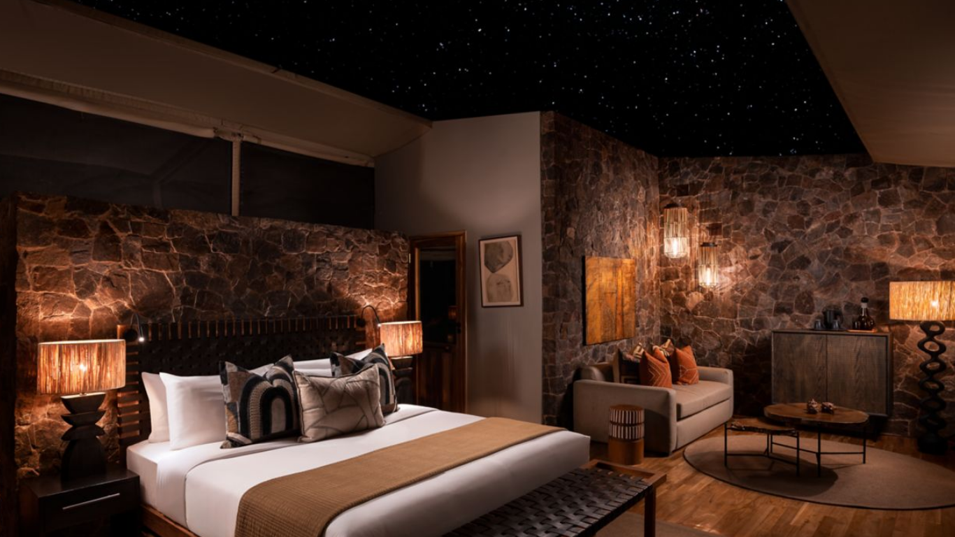 Hotel room with stone wall, king-sized bed, lamps, artwork, sofa, coffee table, and starry ceiling