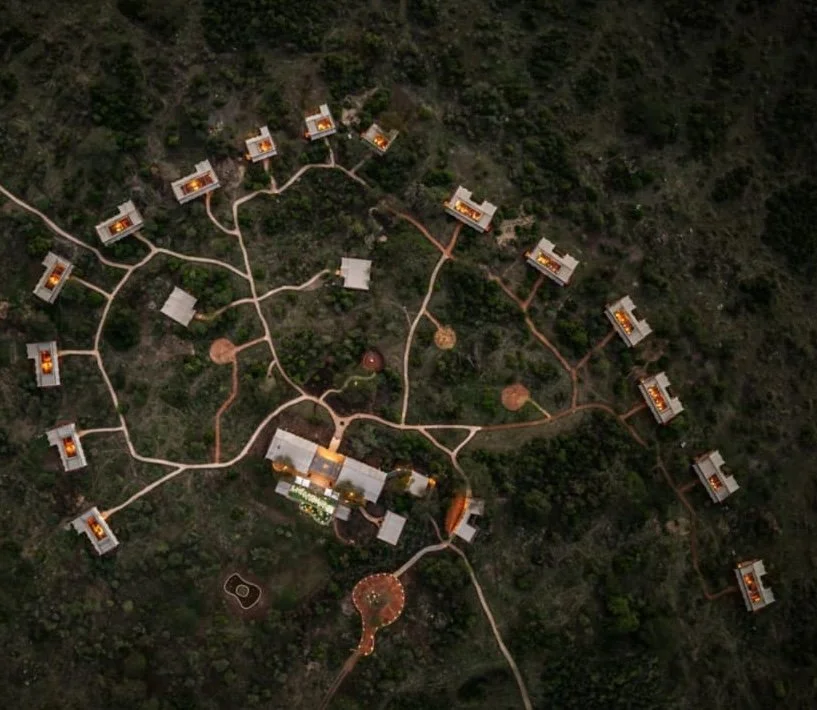 Aerial view of a resort with multiple bungalows connected by walking paths amidst lush greenery.