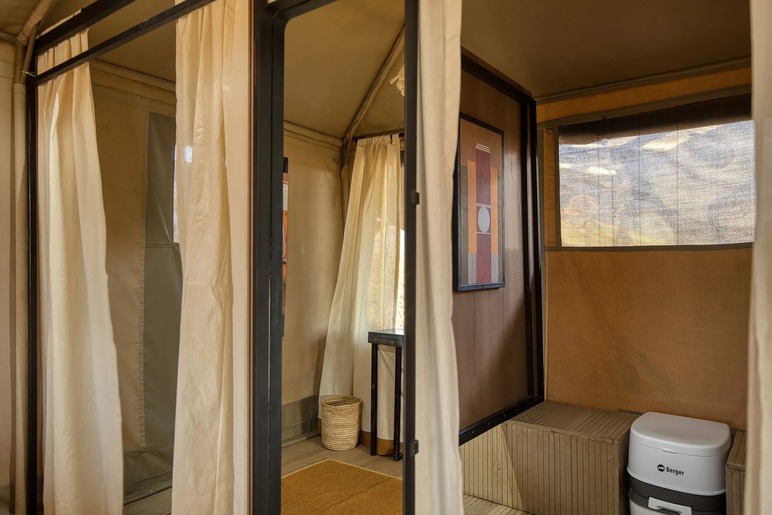 An interior of a fitting room with beige curtains, a mirror, and wooden paneling. There is a small stool, a basket, and a water dispenser visible in the space.