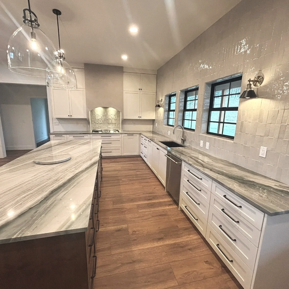 Modern kitchen with white cabinets, marble countertops, wood flooring, and three small windows with black frames.