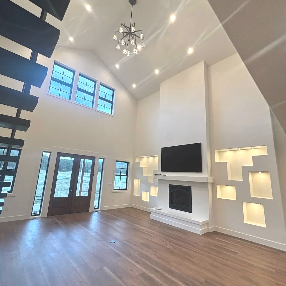 Modern living room with high ceilings, hardwood floors, a contemporary chandelier, a wall-mounted flat-screen TV, a fireplace, and built-in wall niches with lighting.