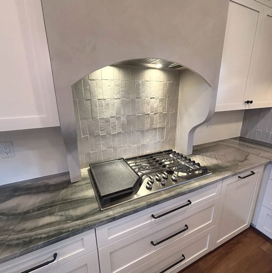 A kitchen countertop with a built-in gas stove, a cast iron griddle, and white cabinetry.