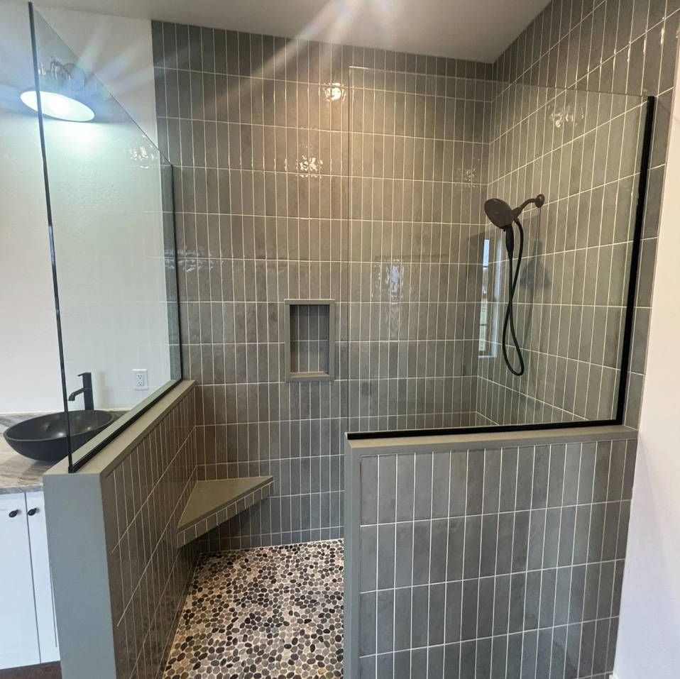 Modern bathroom shower with glass enclosure, gray tiles, pebble floor, and a built-in bench.
