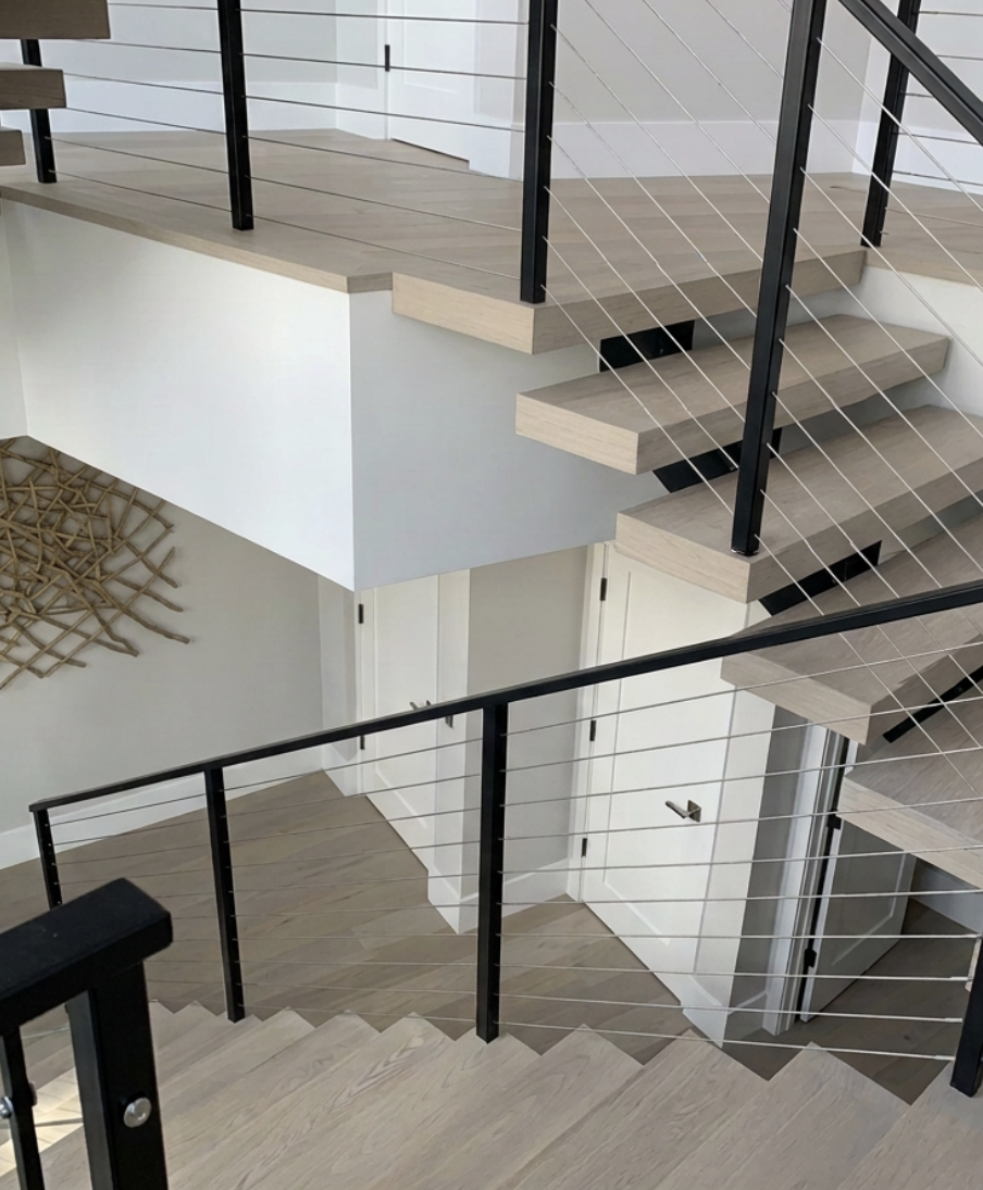 Interior view of a modern staircase with light wood steps and black metal railing with horizontal wires in a contemporary home.