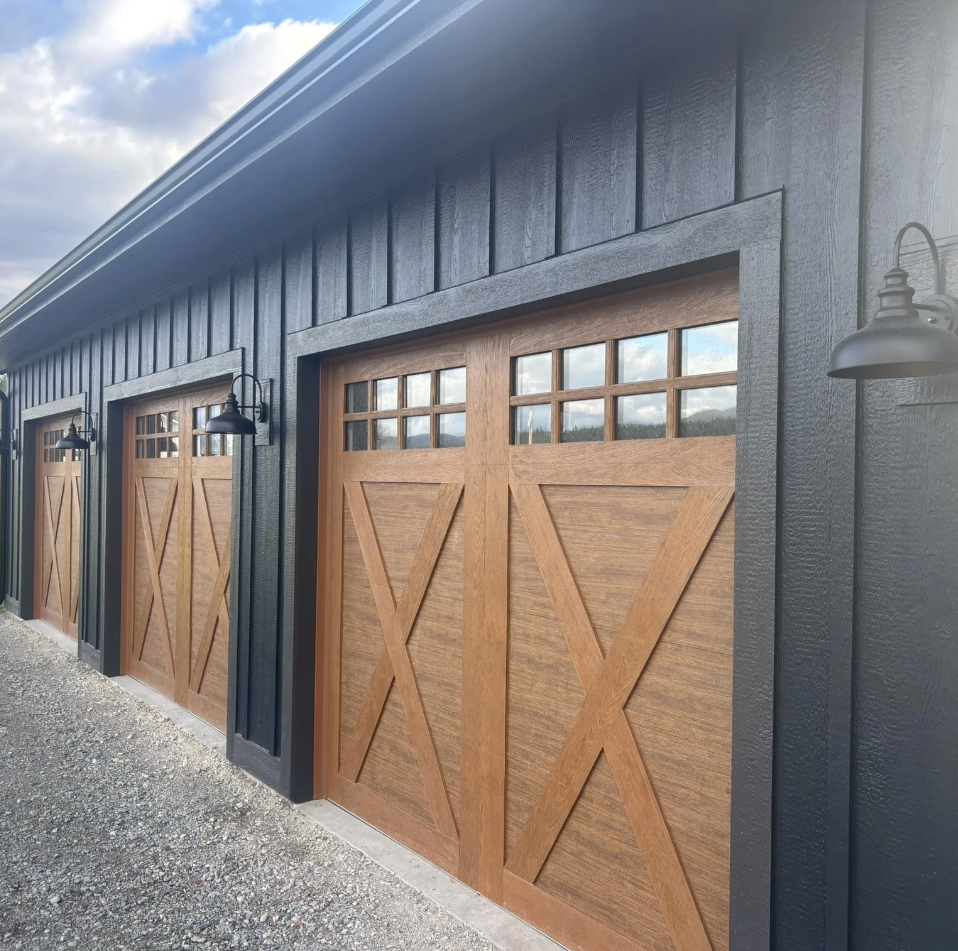 Three wooden garage doors with small windows at the top, set in a black building with exterior lights.