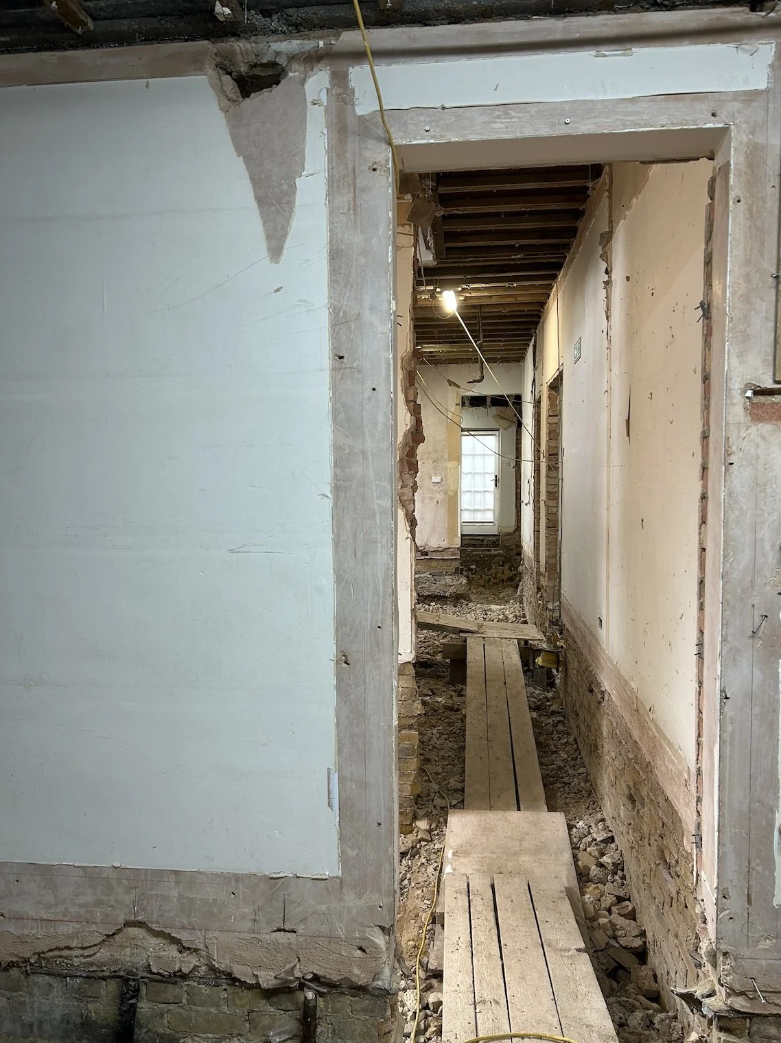 A building interior under renovation, with exposed brick and drywall, wooden planks flooring, and construction wiring.