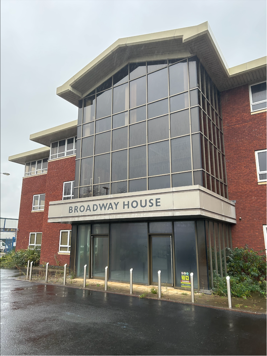 A modern three-story building with large glass windows, a brick exterior, and a sign that reads 'Broadway House' at the entrance.