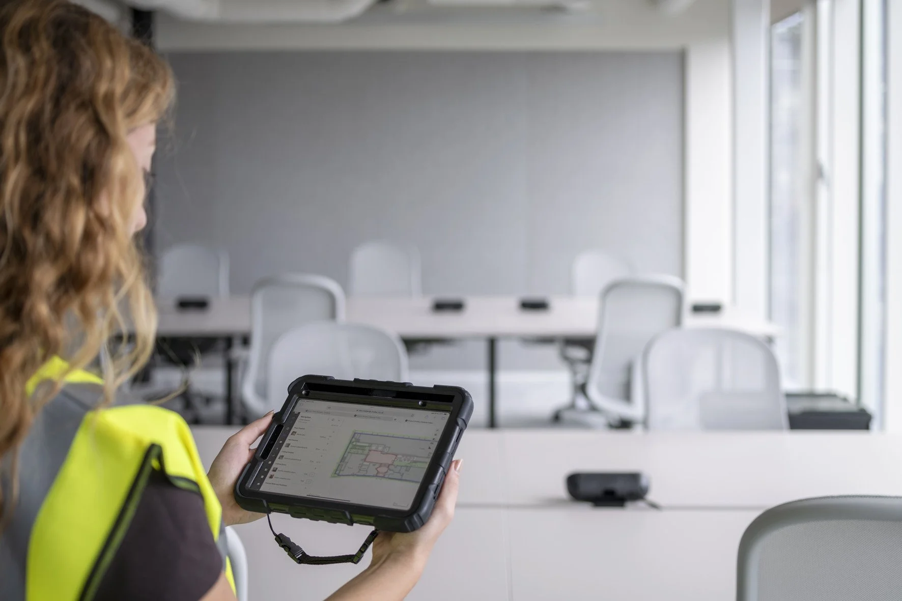 Auditor in a yellow safety vest taking a survey of materials in an office