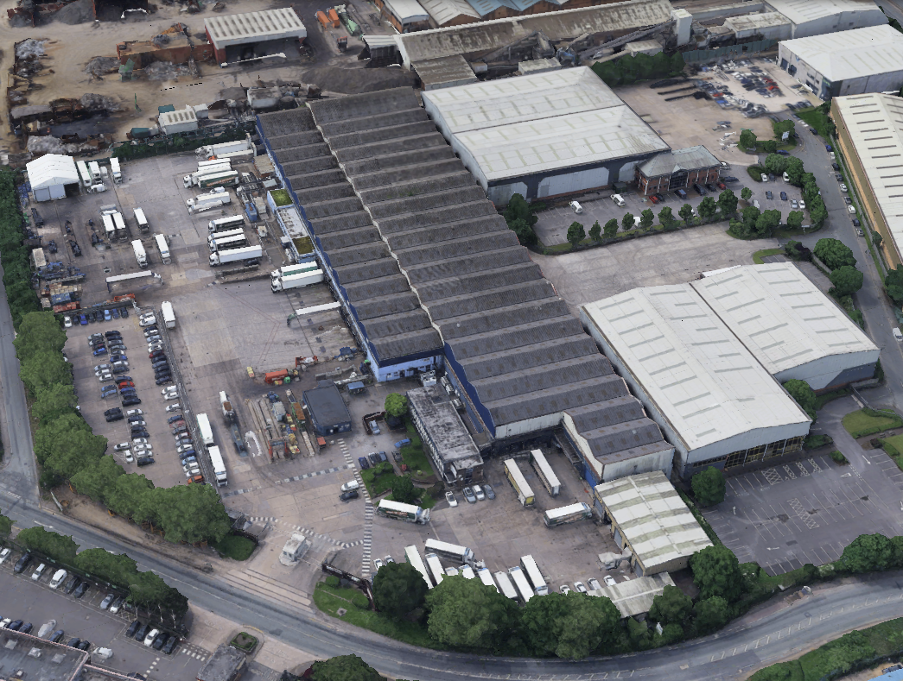 Aerial view of an industrial complex with several warehouses, parking lots, and trucks parked in designated areas.