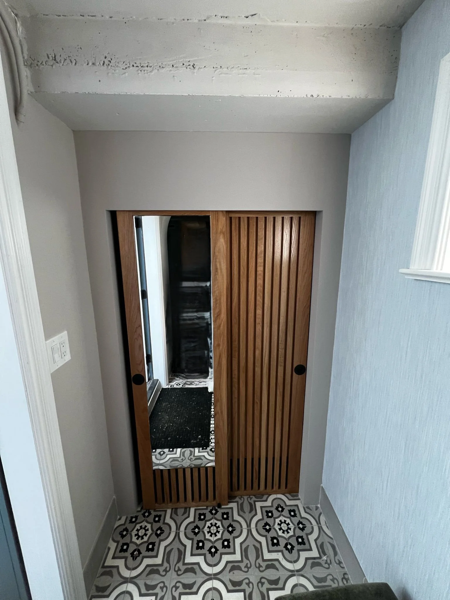 New coat closet in new mudroom with custom wood slat doors and new tiled floor