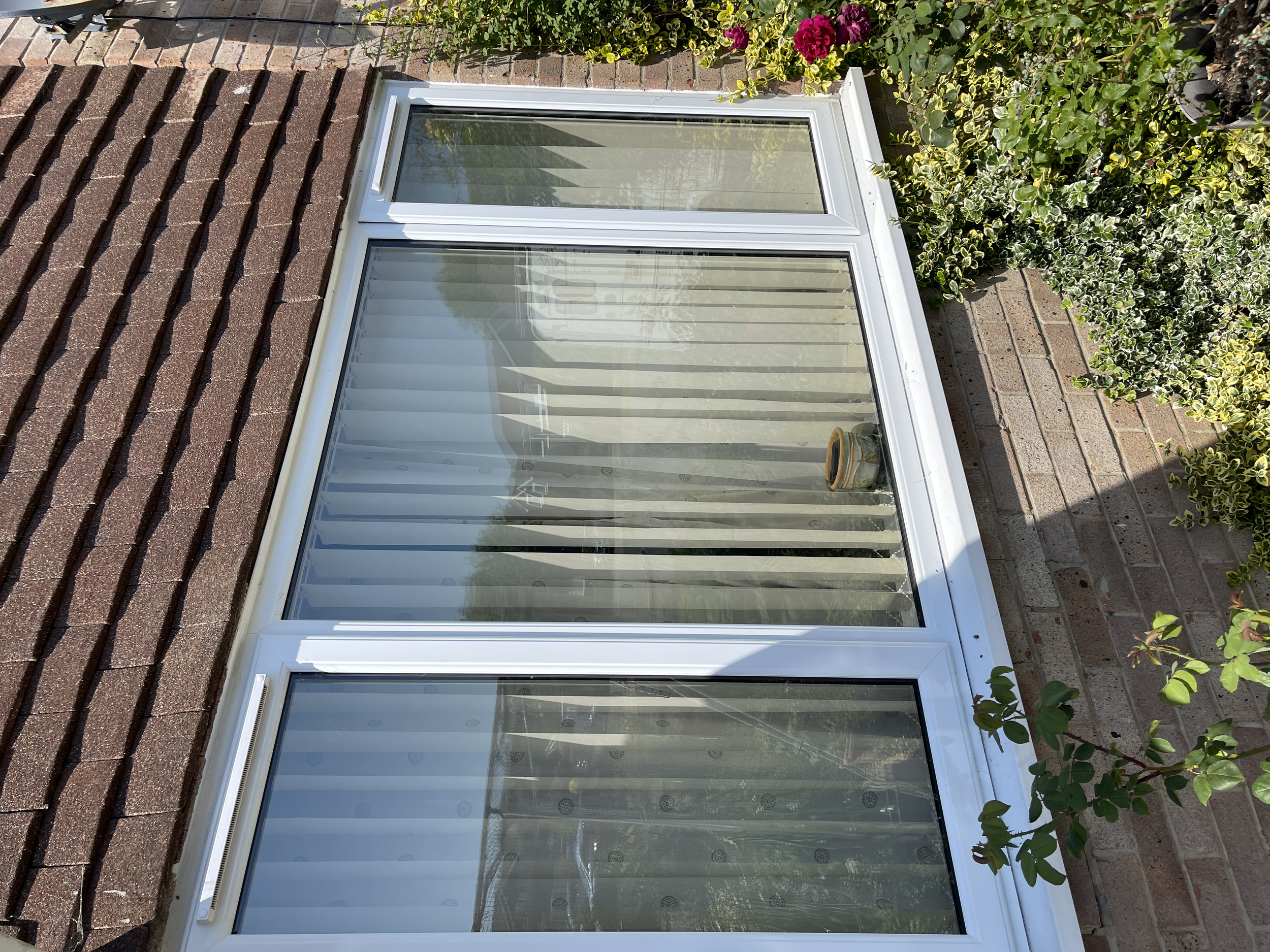 A set of glass sliding doors with sheer curtains, surrounded by brick house walls and greenery including bushes with pink and green leaves.