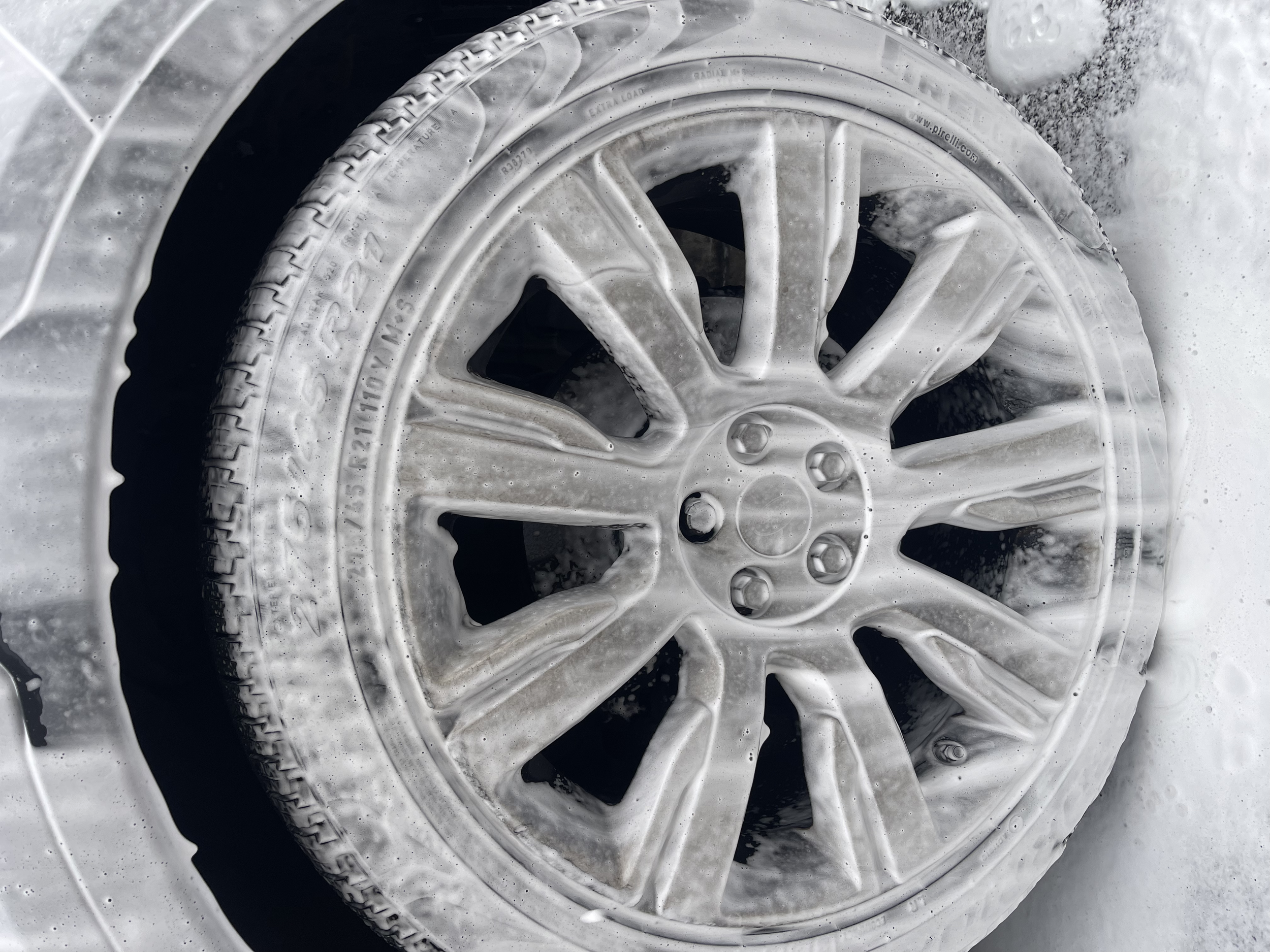 Close-up of a car wheel covered in soap suds during washing.