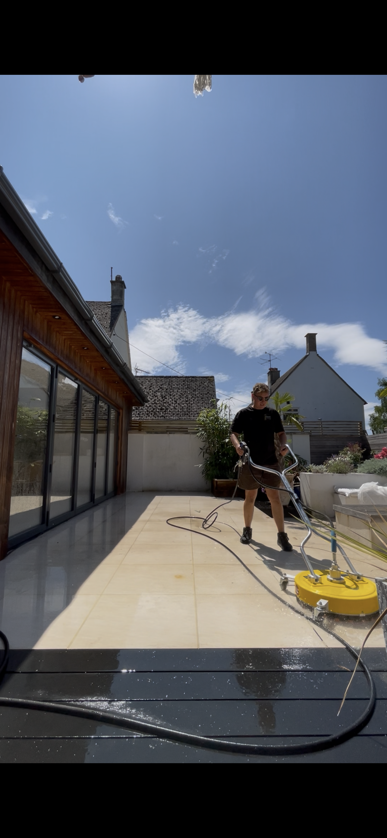 Man cleaning the tiled outdoor patio using a floor cleaning machine on a sunny day.