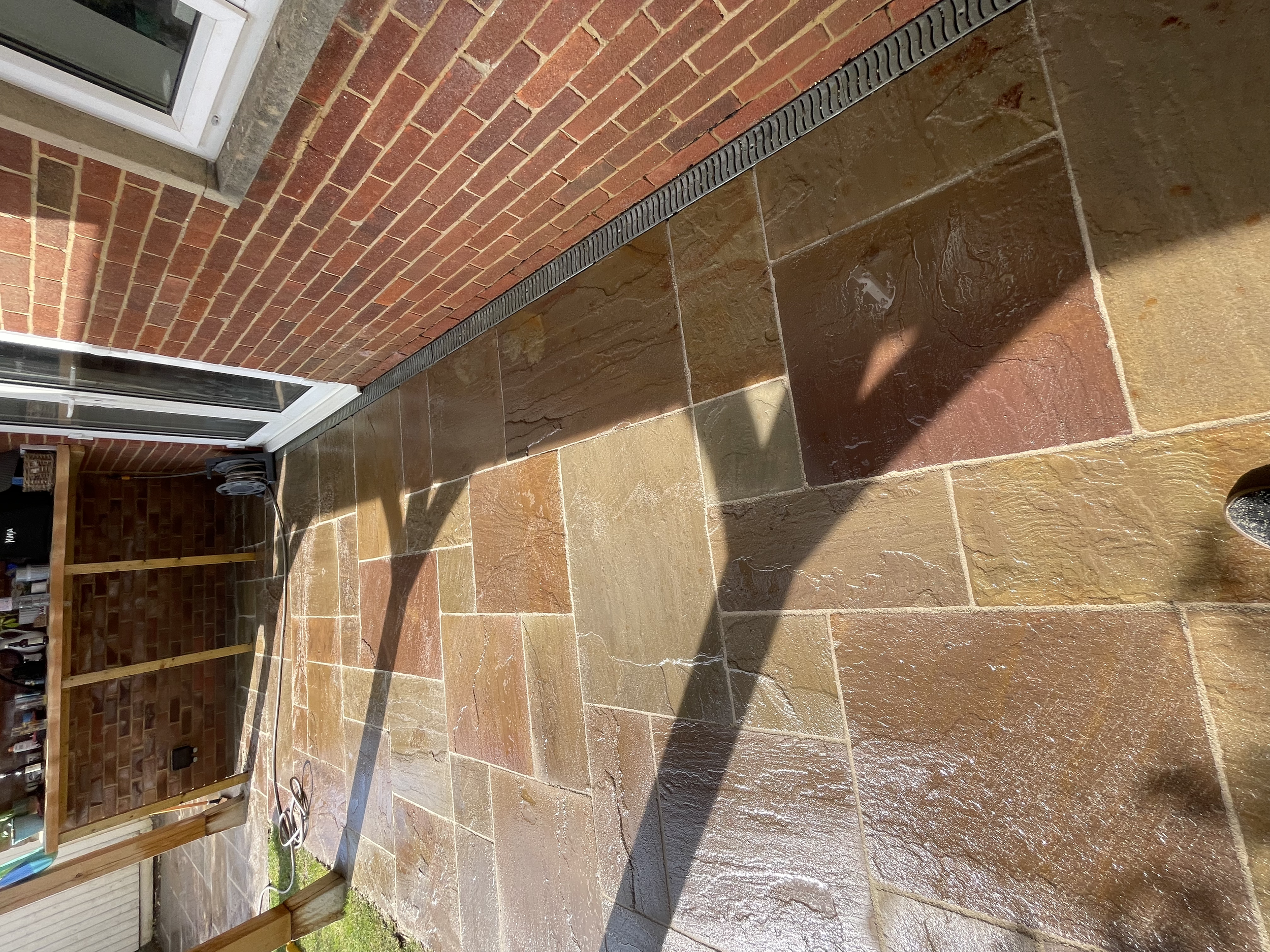 A brick exterior wall and a wet tiled patio area, part of a backyard or porch.