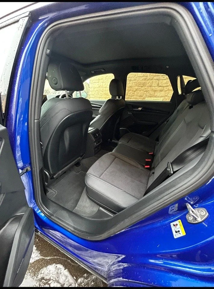 The interior of a blue SUV showing the backseat with black seats and an open door.