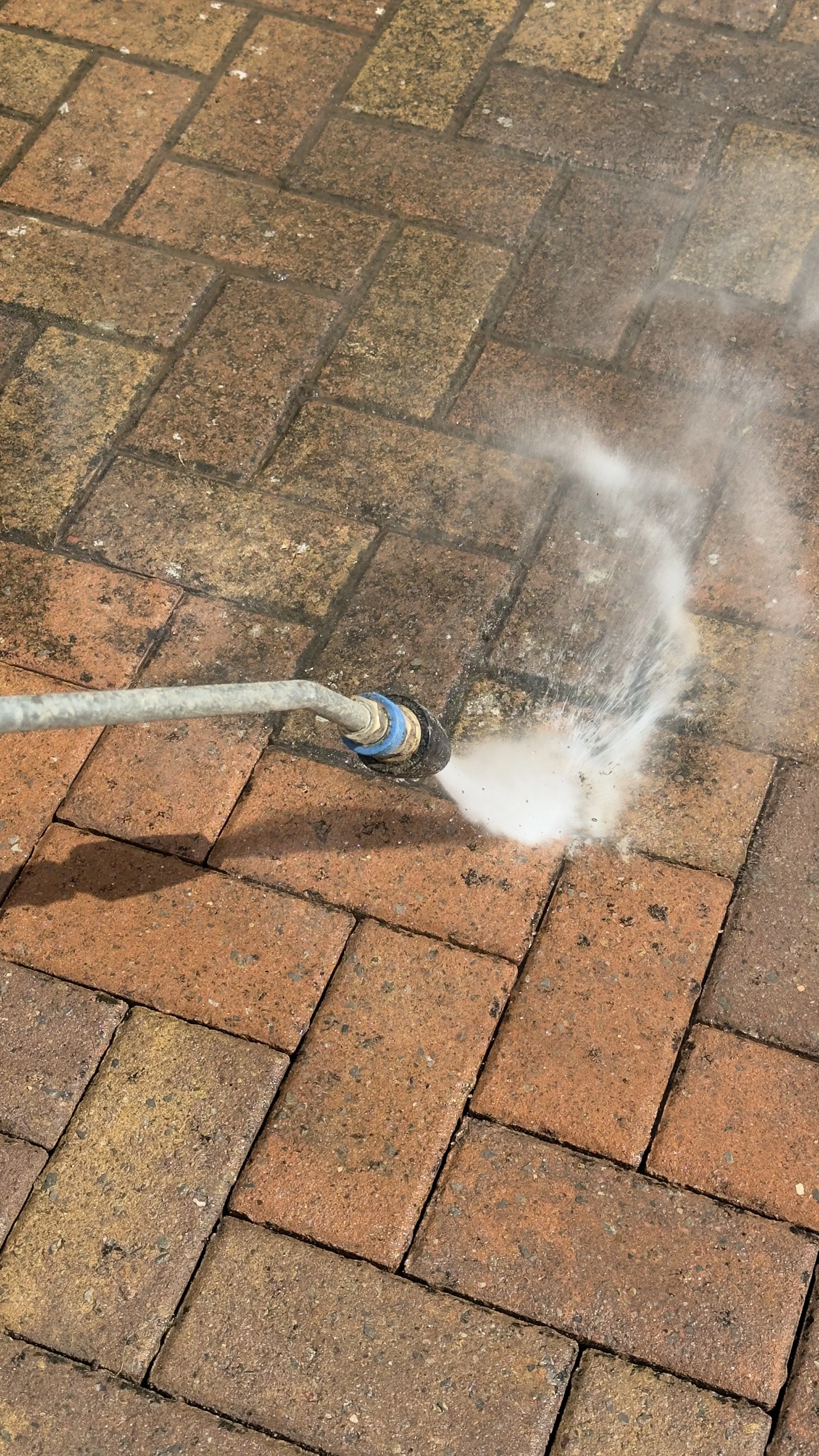 A pressure washer spraying water onto a brick pavement.
