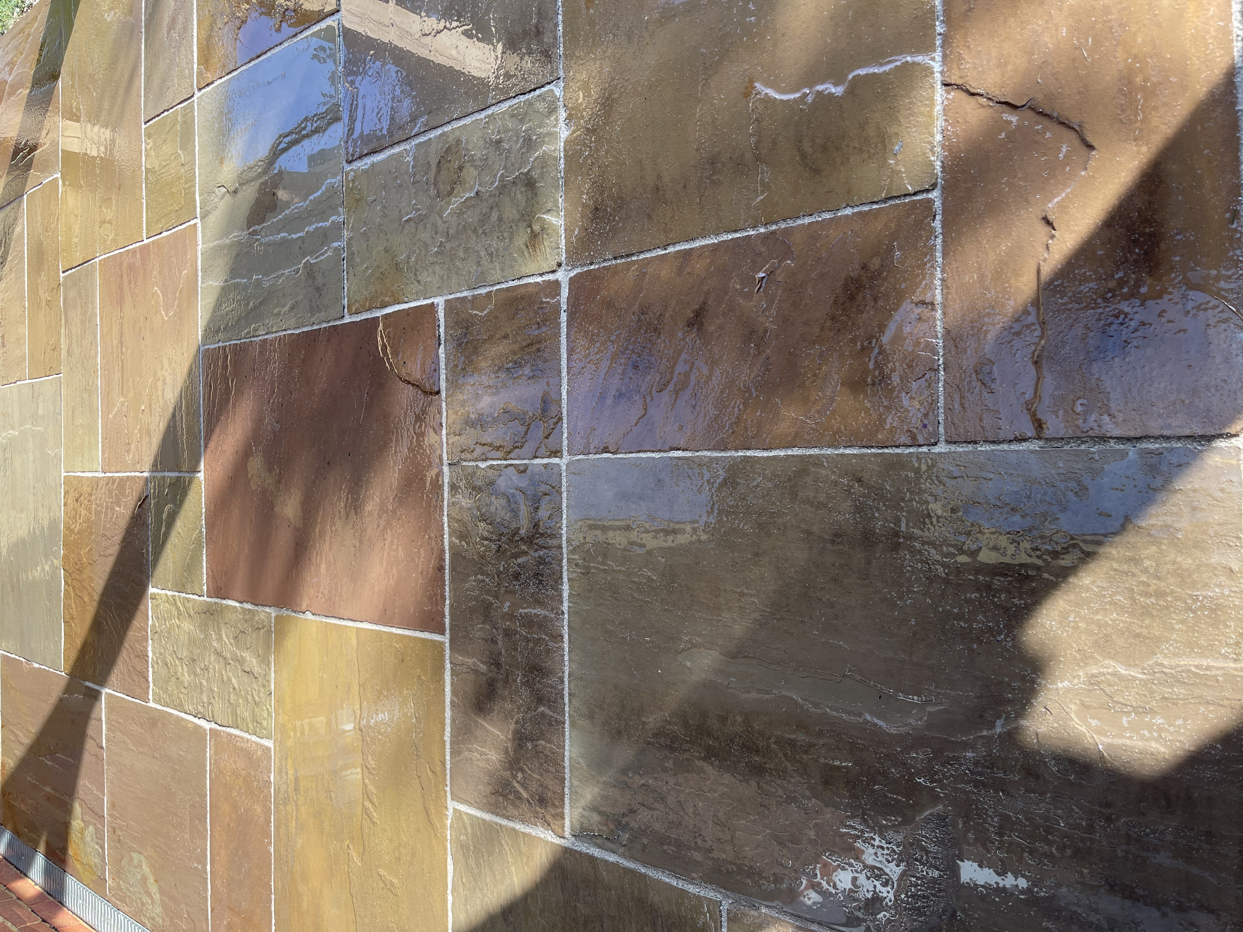 Close-up view of a wet, multicolored natural stone tile wall with visible grout lines.