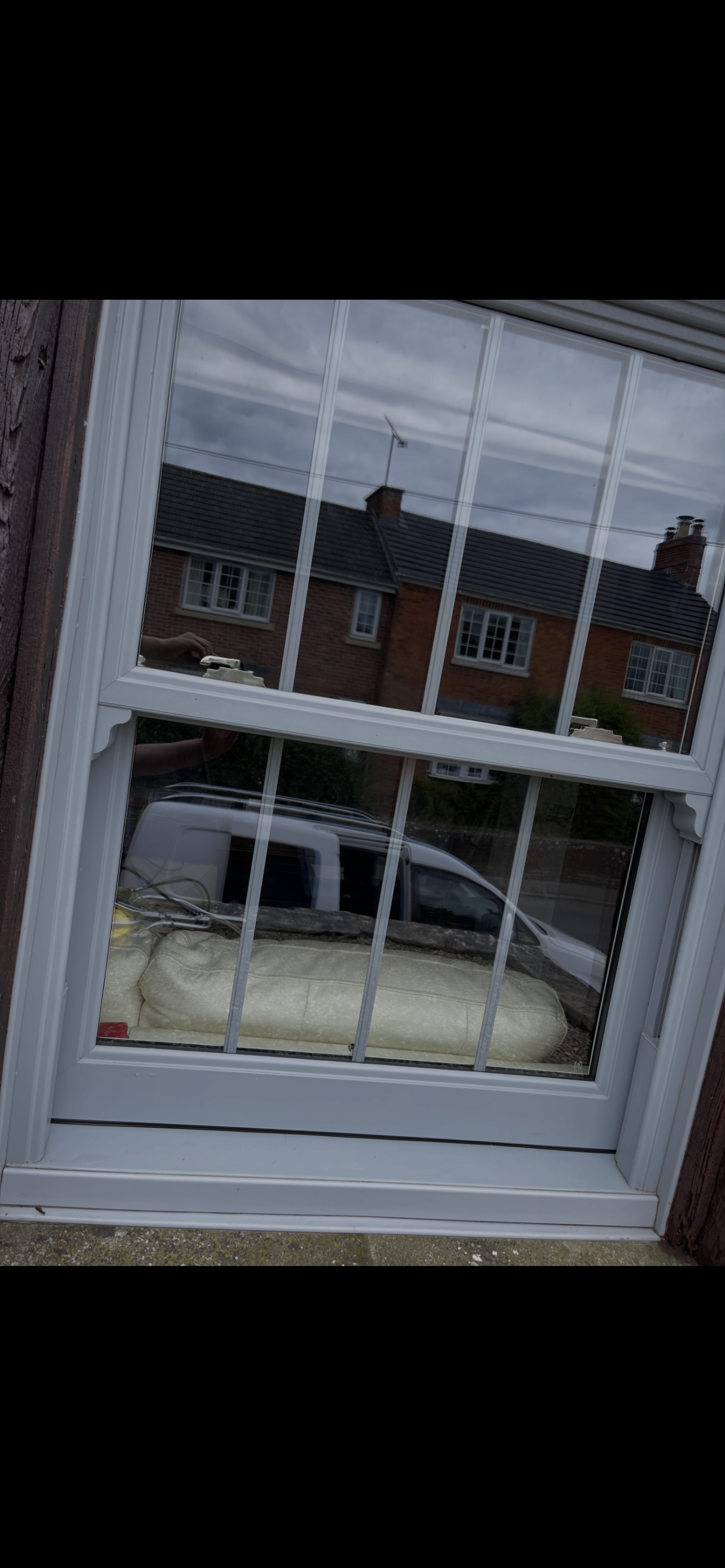Reflection of houses and a cloudy sky in a window with bars, showing a beige pillow and some objects inside a house.