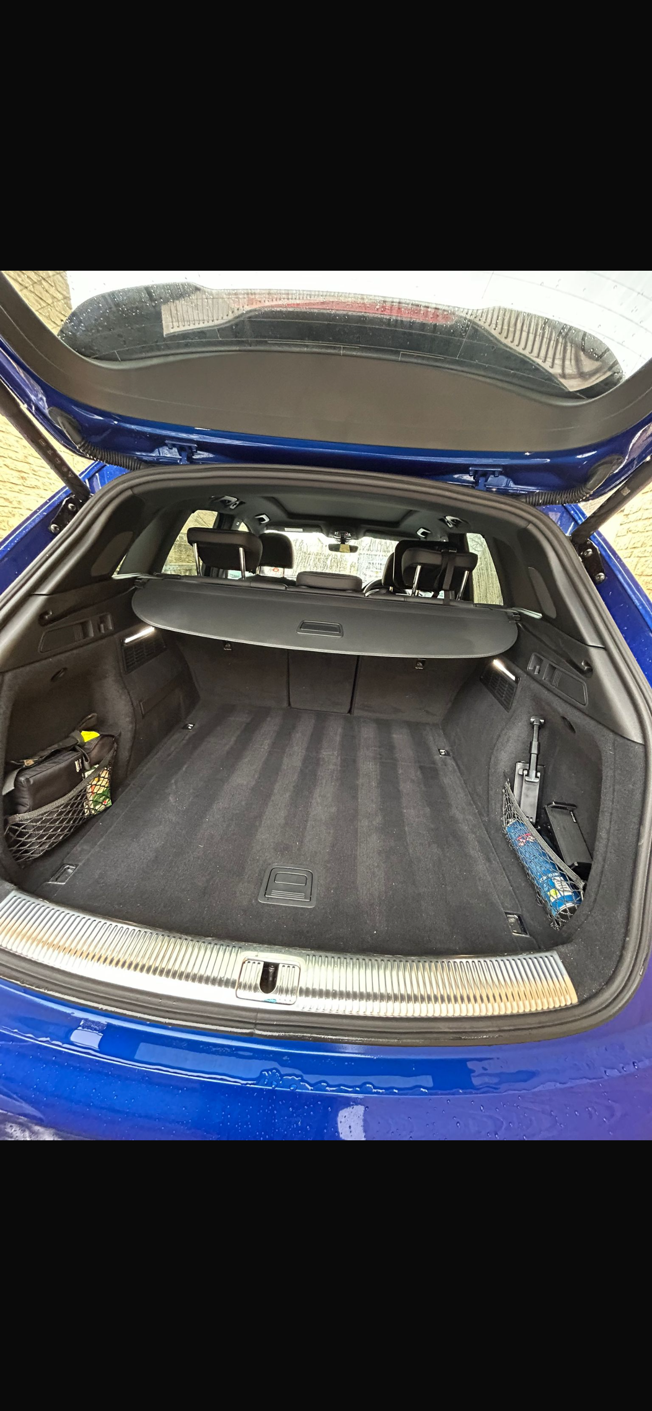 Open blue SUV showing empty cargo space with storage net on left and small compartment on right, rubber cargo cover, and rear seats.