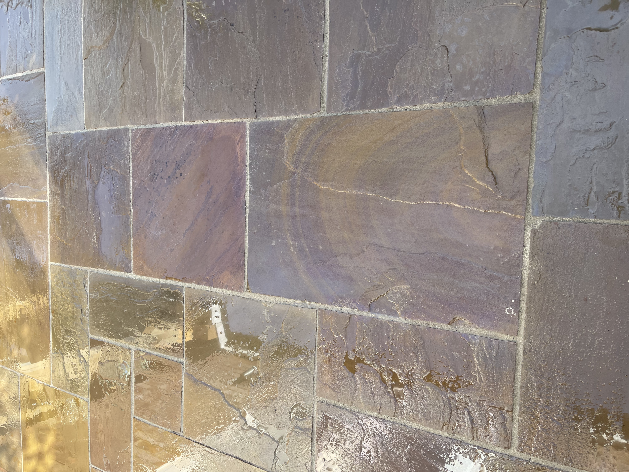 Close-up of a stone tile floor with earthy tones and irregular surface textures, some with visible cracks and variations in color.