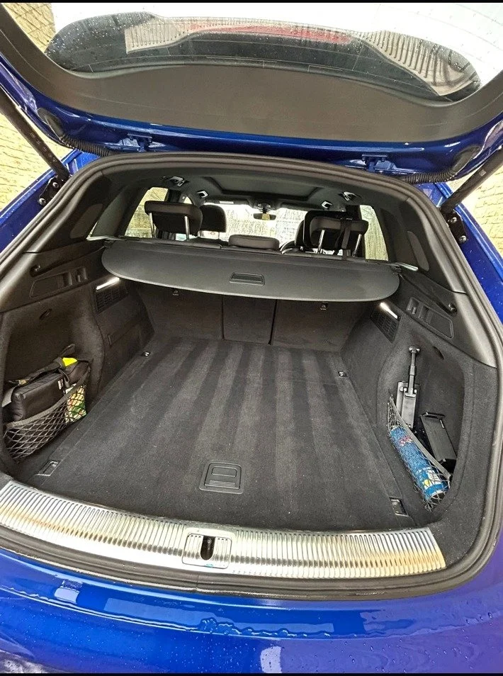 Open rear cargo area of a blue SUV with a black cargo cover, side storage nets, a tool kit, and a rolled-up item on the right side.