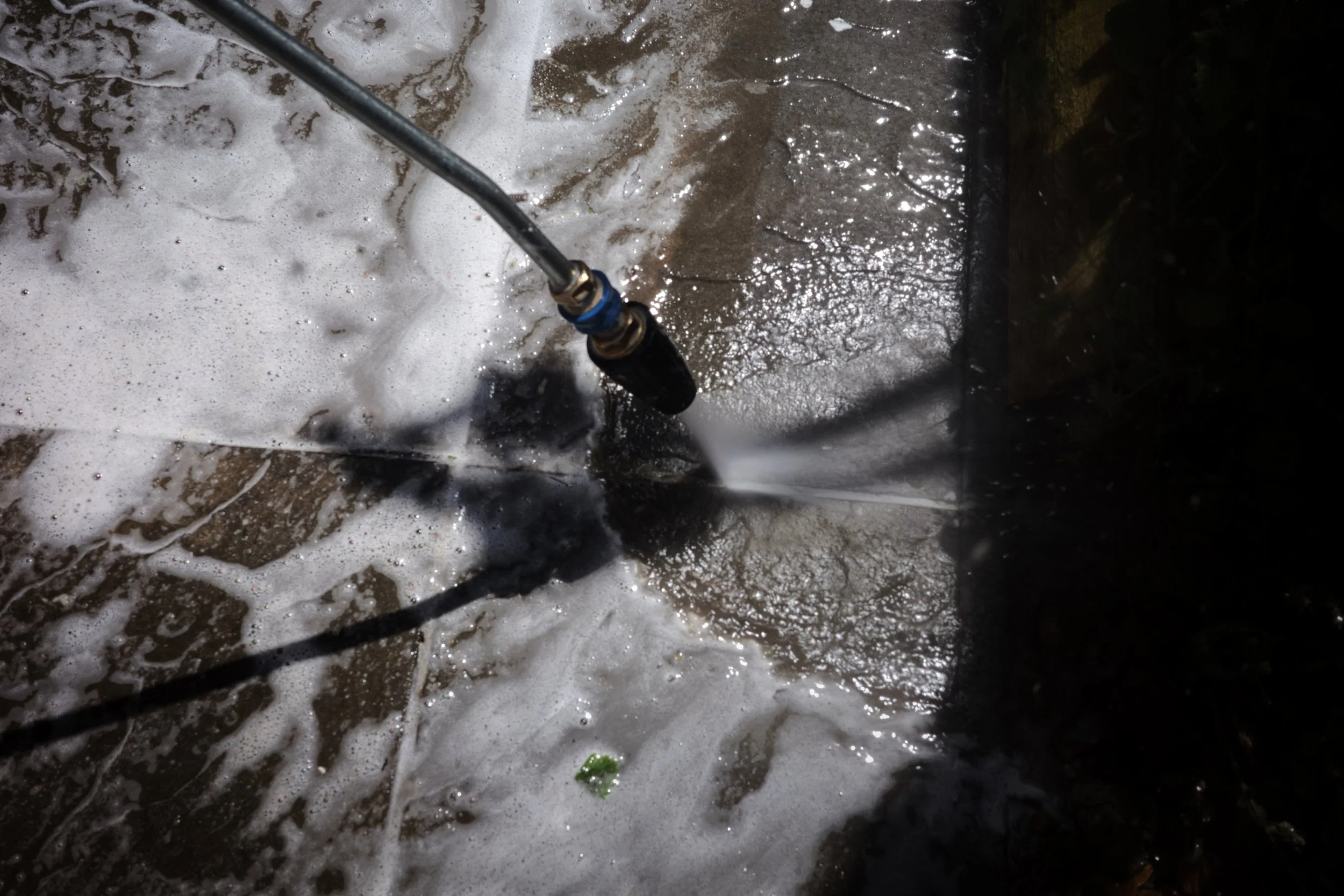 A person power washing a concrete surface outdoors, creating foam and water spray with a high-pressure nozzle.